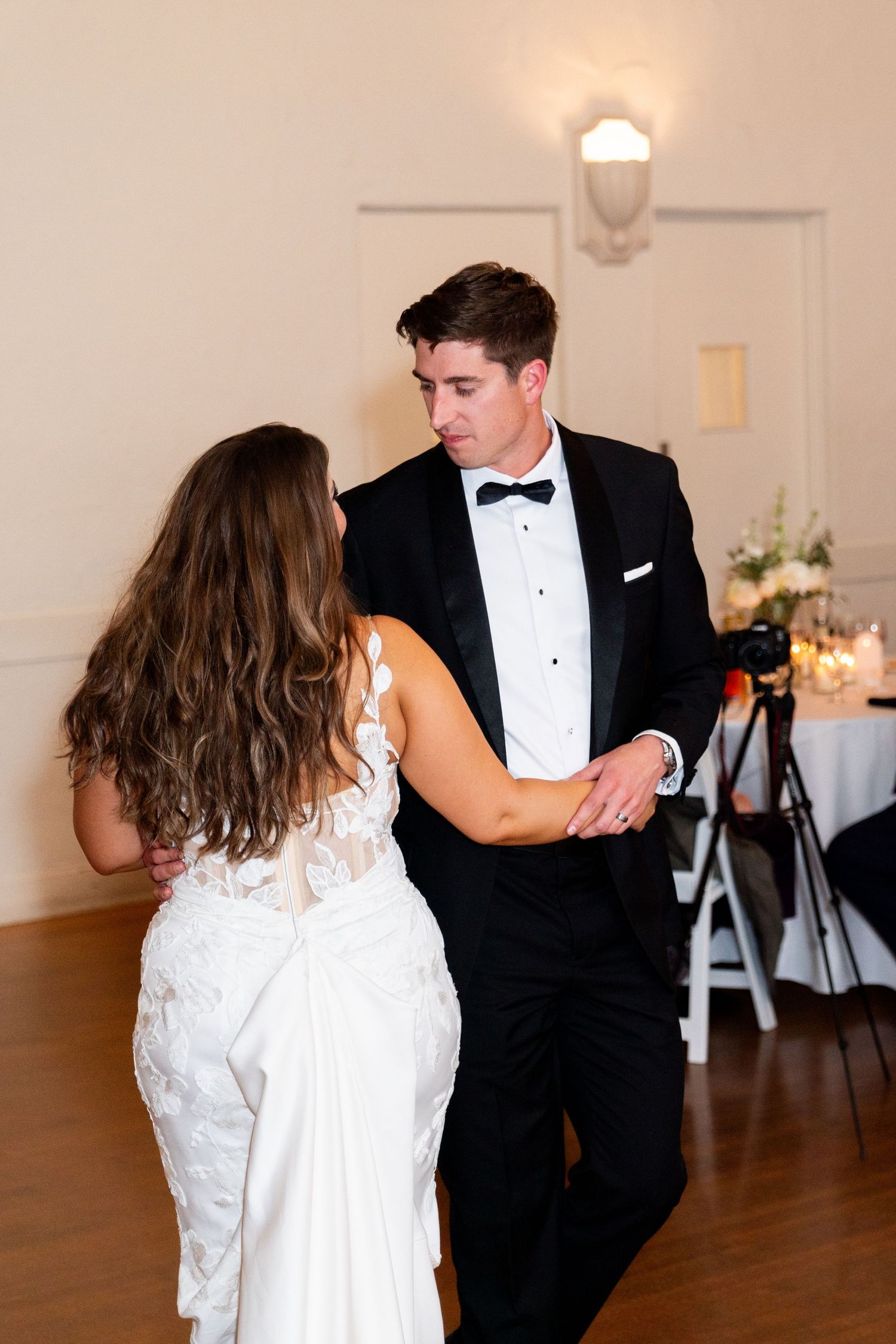 A couple dancing in formal attire on a wooden floor at an indoor venue.