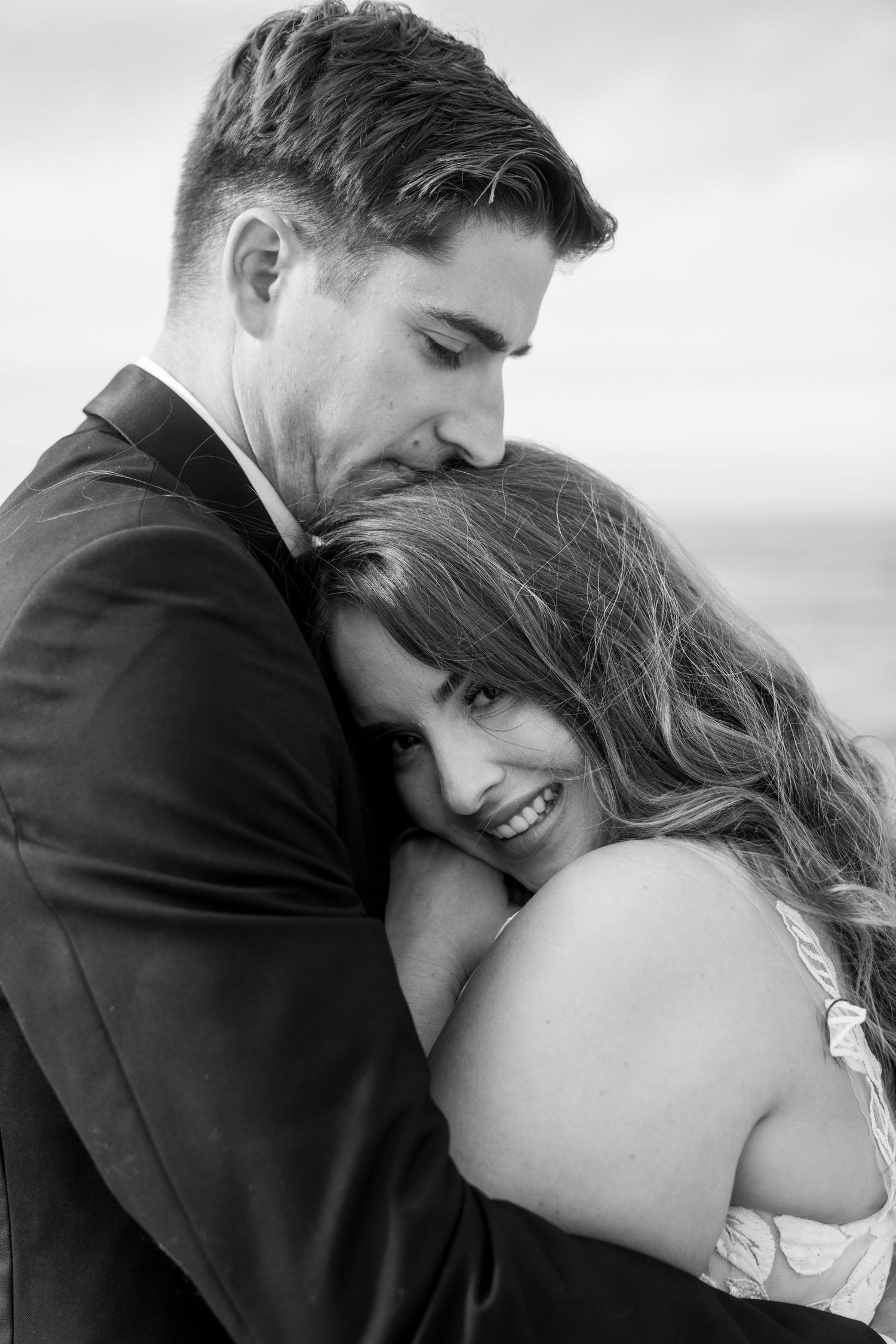Intimate black and white portrait of a couple sharing a tender embrace in formal wedding attire.