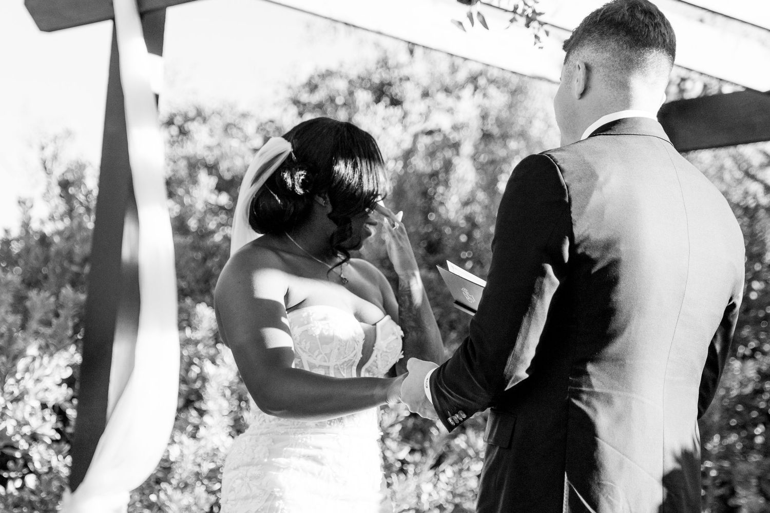 Black and white photo capturing emotional wedding ceremony moment outdoors.