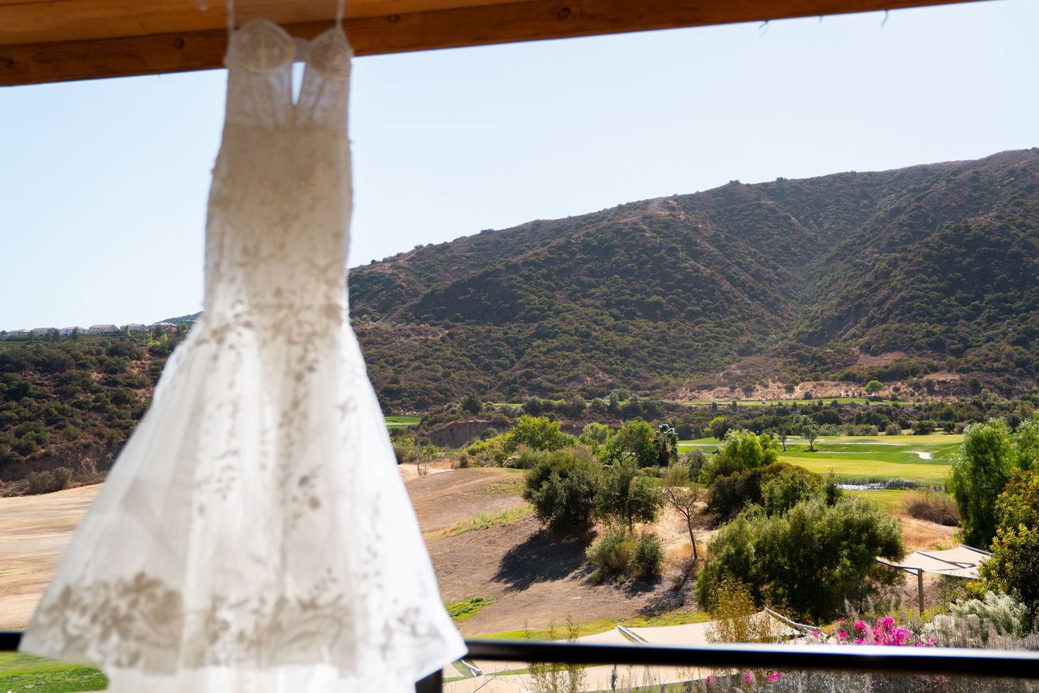 White wedding dress hanging with scenic mountain landscape and golf course view in background.