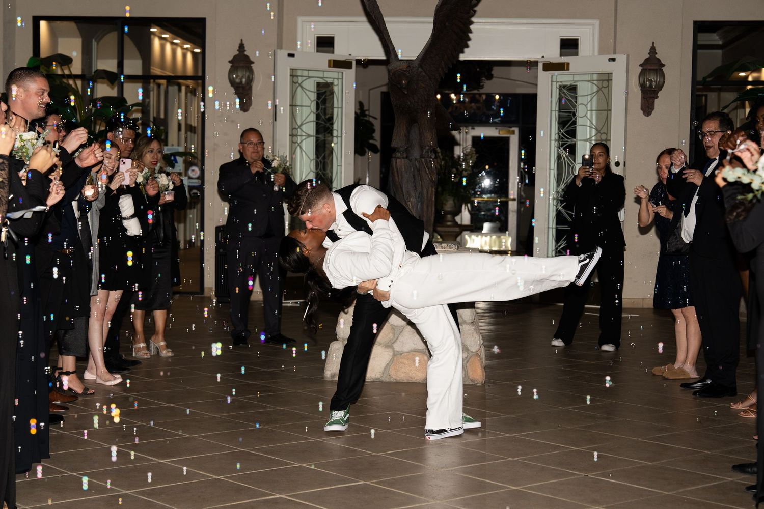 Wedding couple performs dramatic dance dip move while guests throw confetti in elegant reception venue.