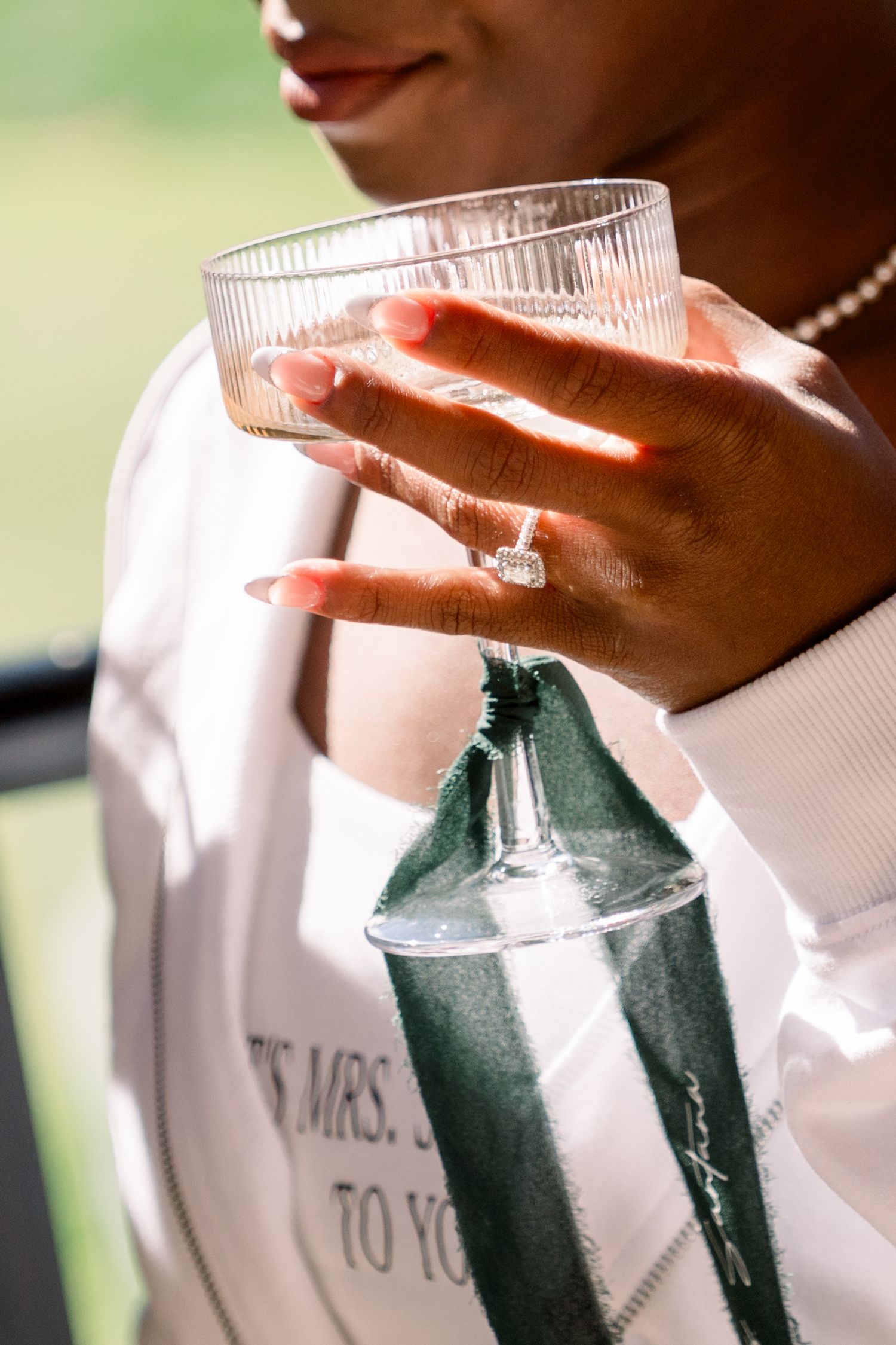 Close-up of a hand holding a glass with an engagement ring on display.