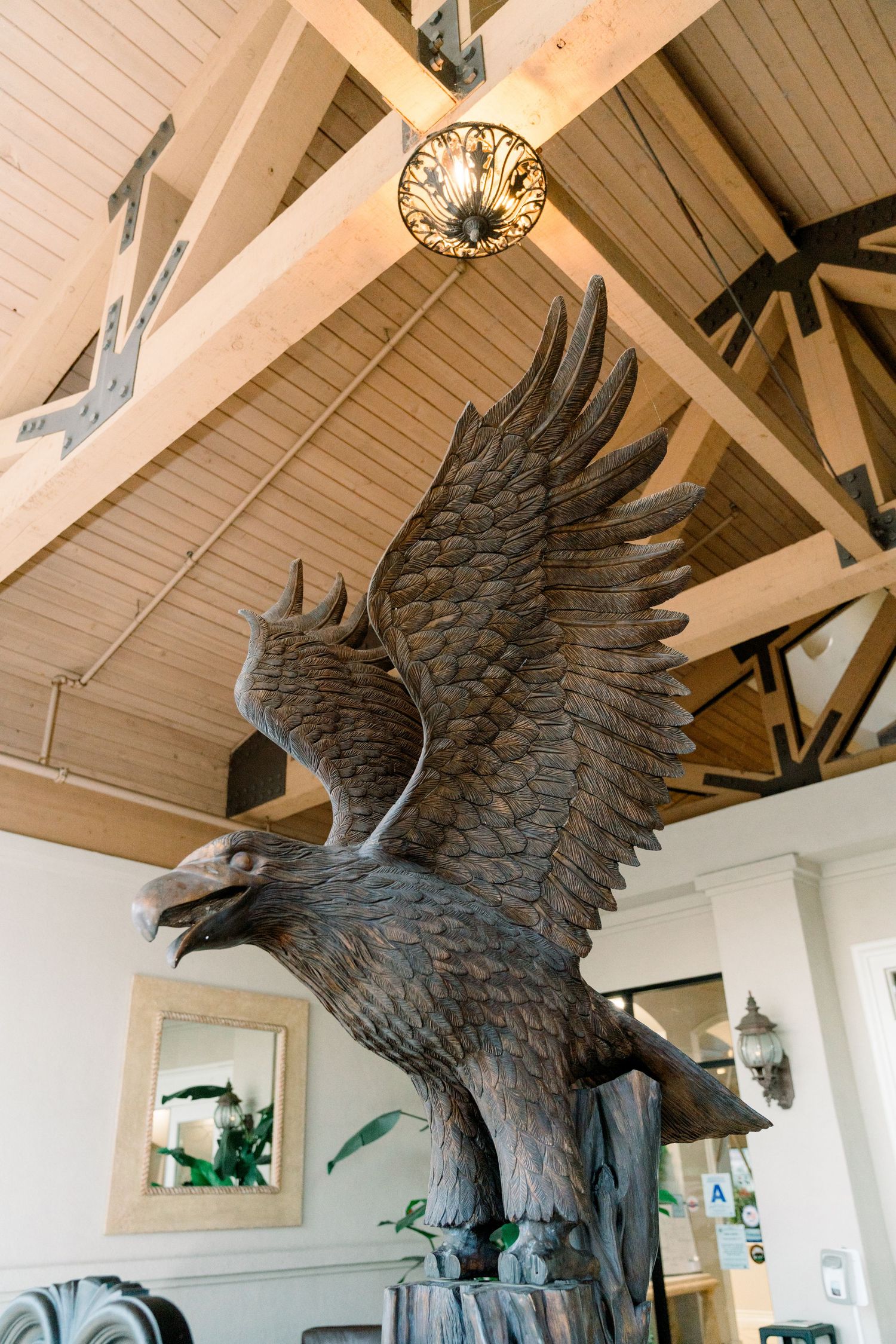 Large decorative bronze eagle sculpture mounted on white wooden beams in an interior space with vaulted ceilings.
