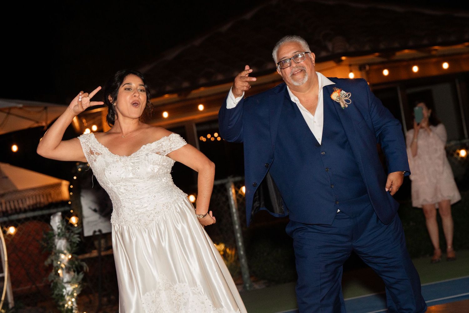 Wedding couple dancing energetically at nighttime outdoor reception.