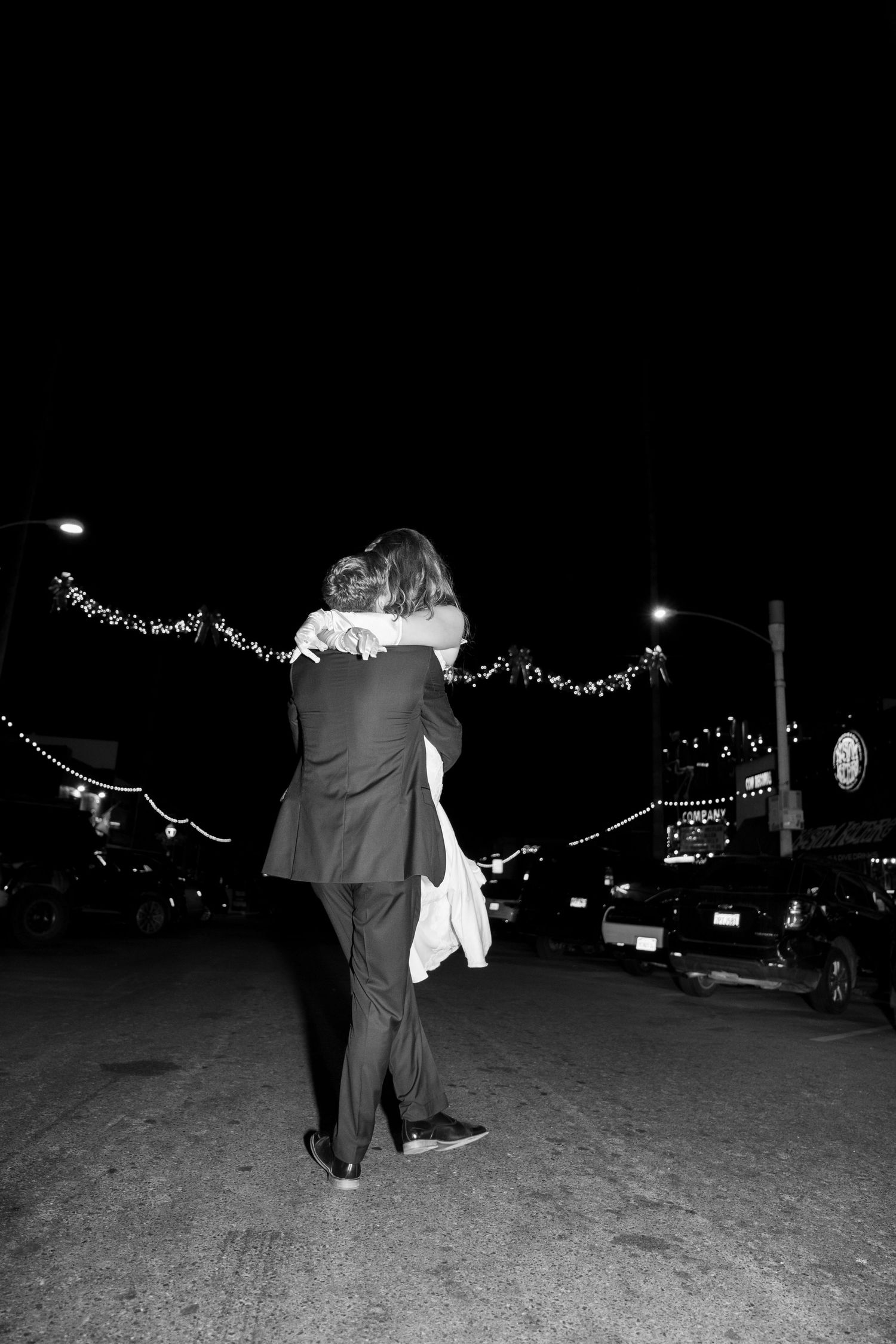 A romantic black and white photo of a couple embracing under twinkling lights at night.