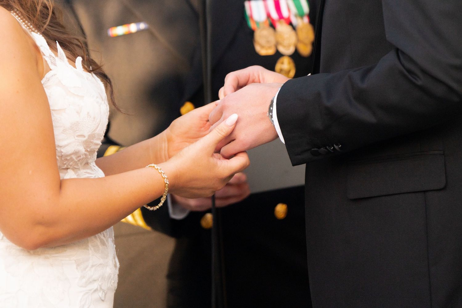 A close-up view of hands exchanging wedding rings during a marriage ceremony with medal decorations in the background.