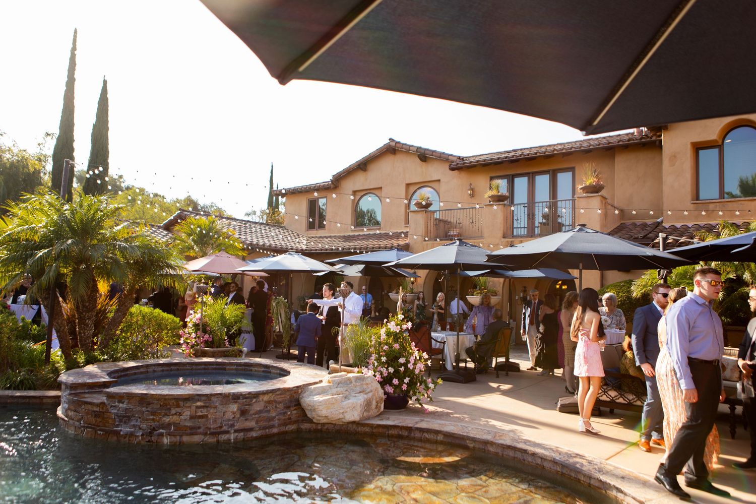 Mediterranean-style venue with terra cotta building, outdoor patio, umbrellas and decorative water feature.