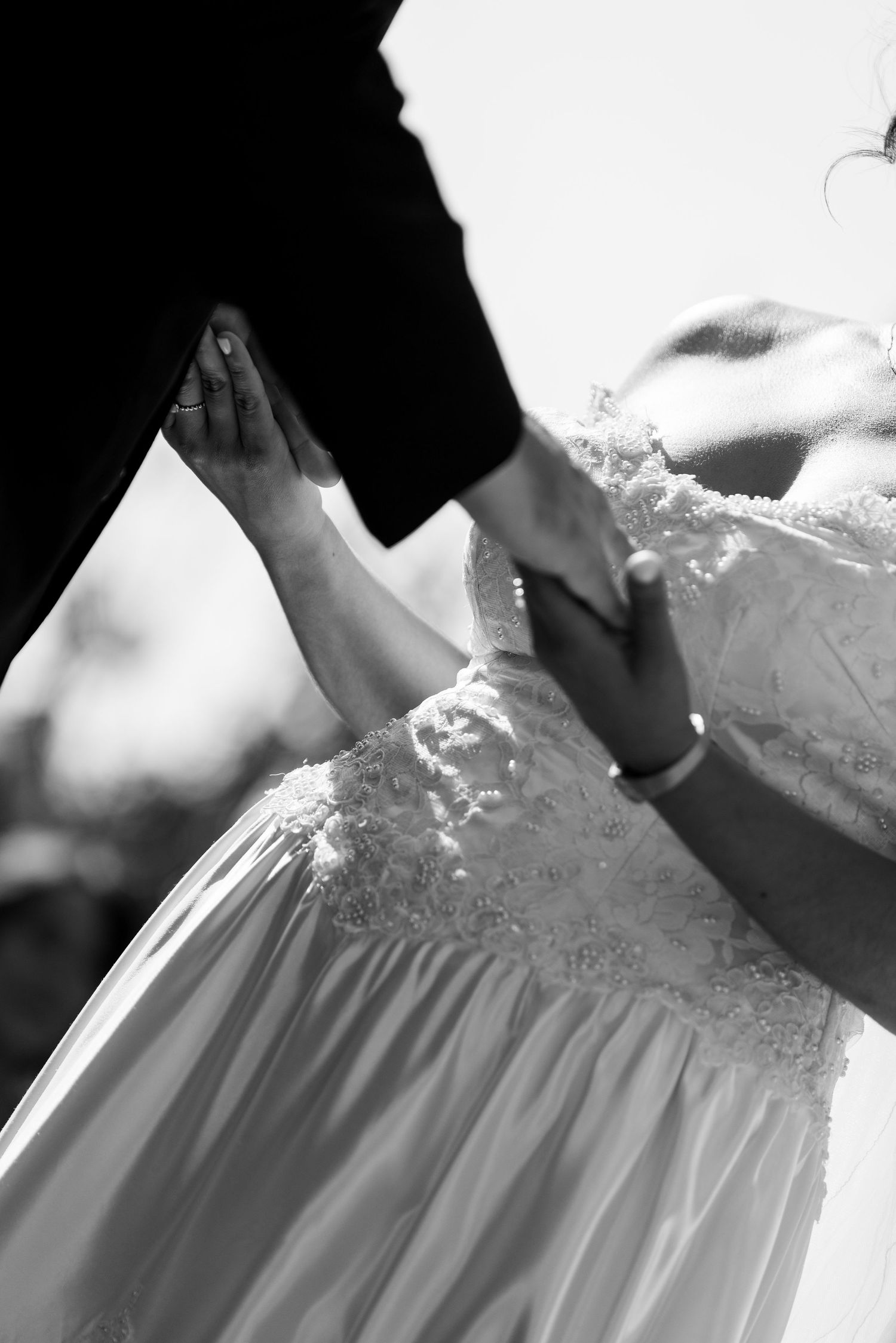 Close-up black and white detail of a wedding dress being adjusted, showing delicate lace and fabric details.