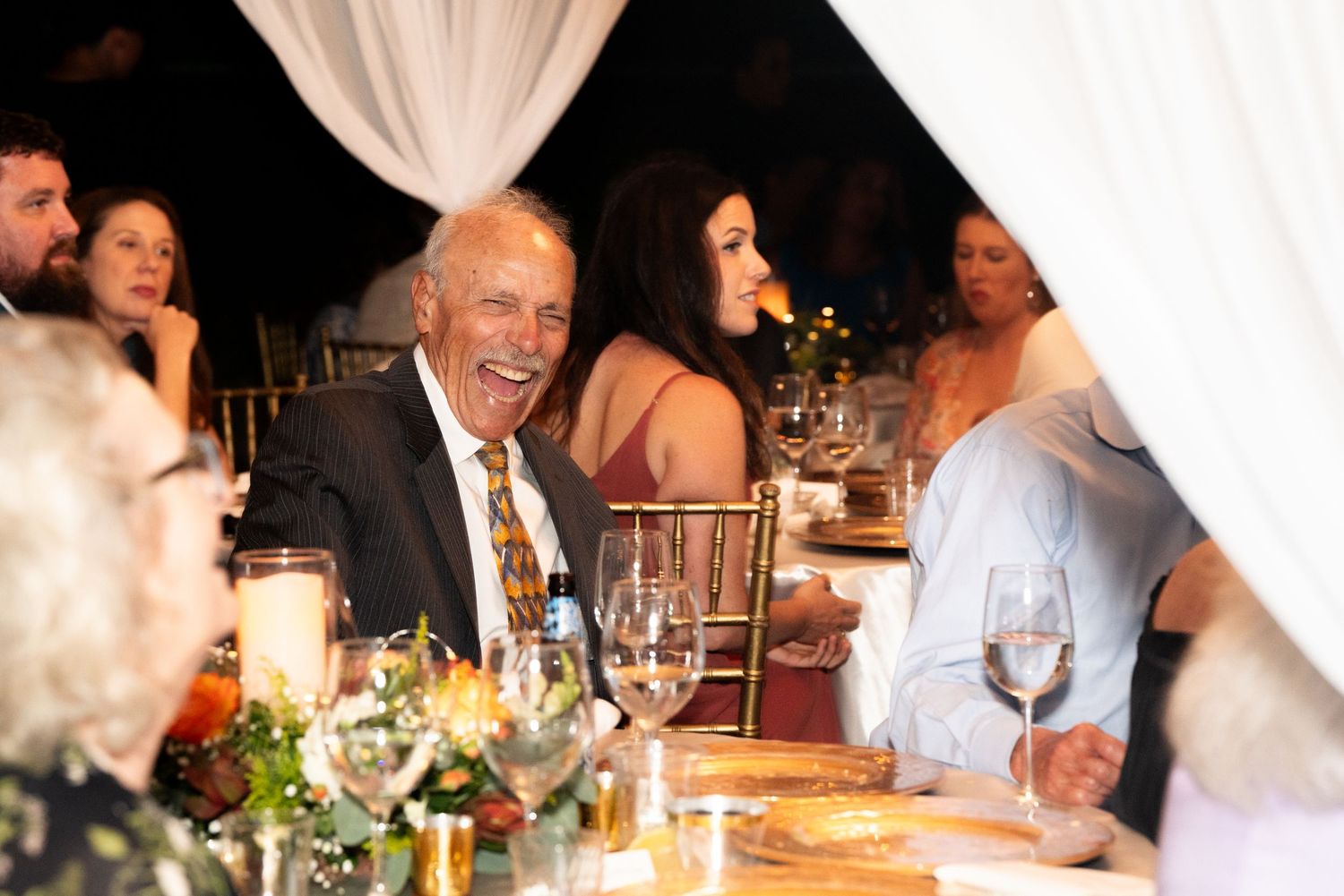 Wedding guests share laughter around an elegantly decorated candlelit dinner table.