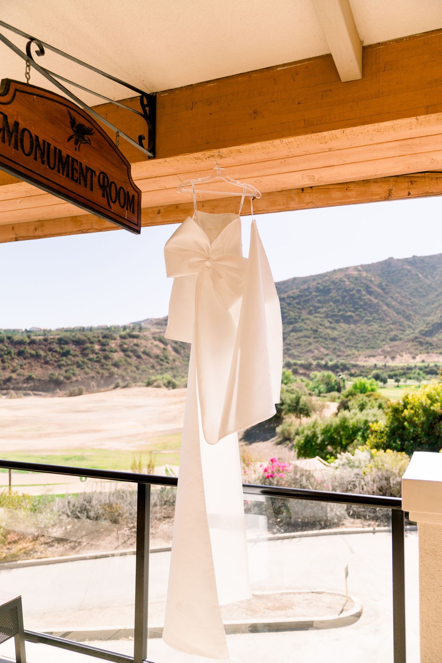 White wedding dress hanging on wooden porch with scenic mountain landscape view in background.