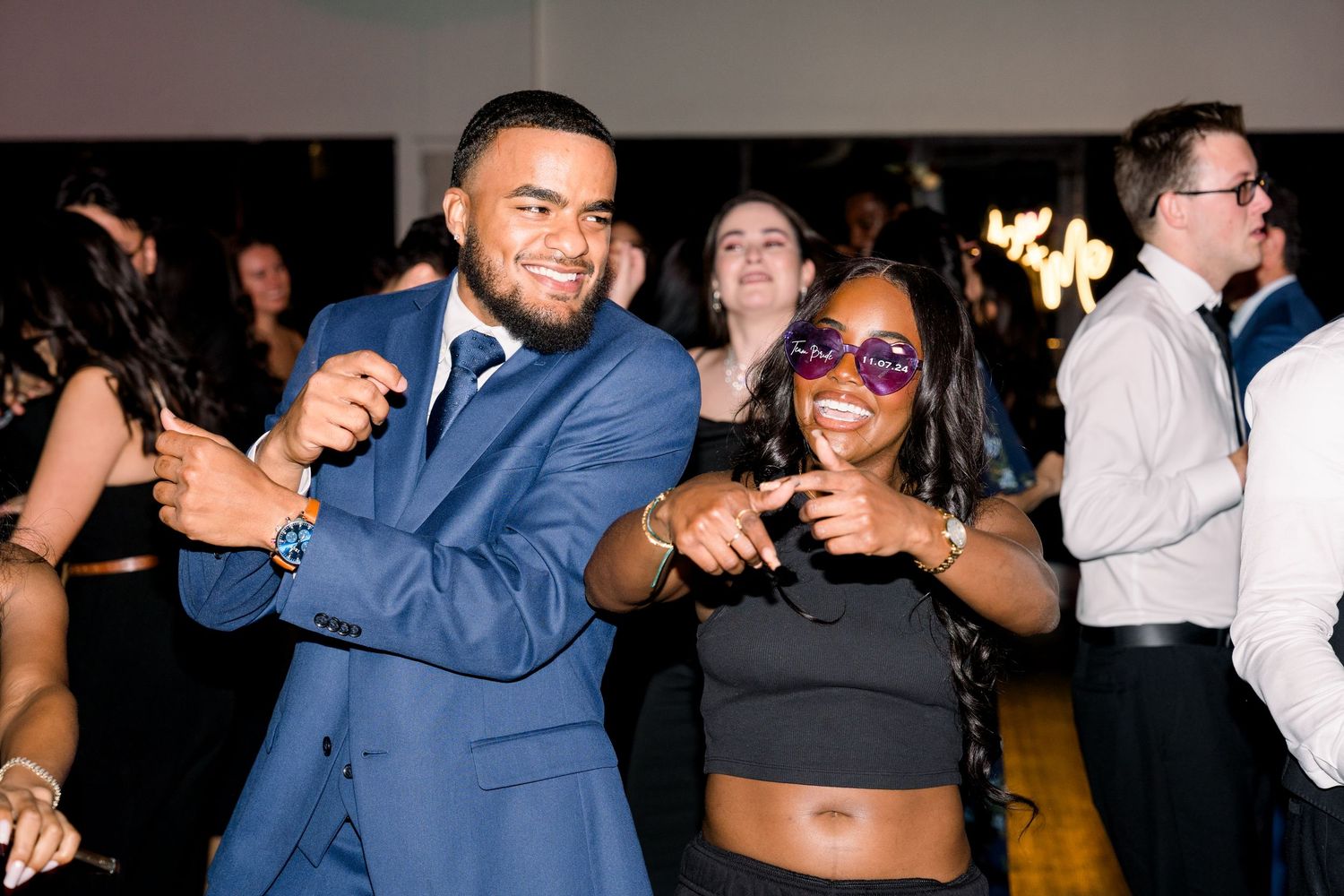 Party guests dance energetically at a wedding reception under dimmed lighting.