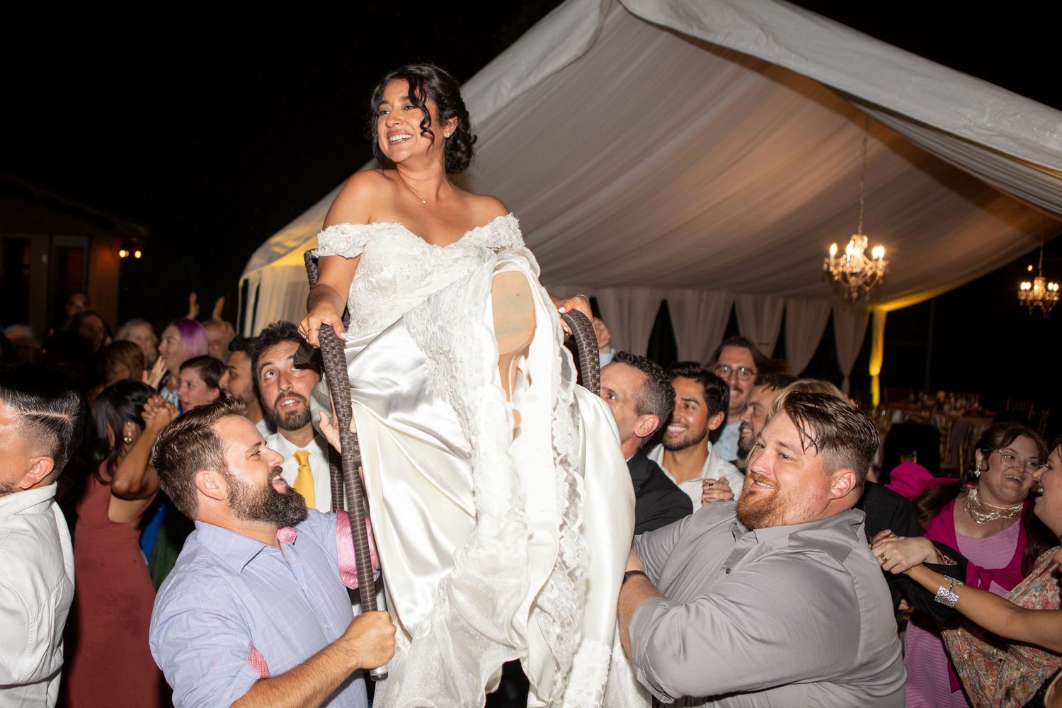 Wedding celebration with the bride being lifted up by guests during reception festivities.