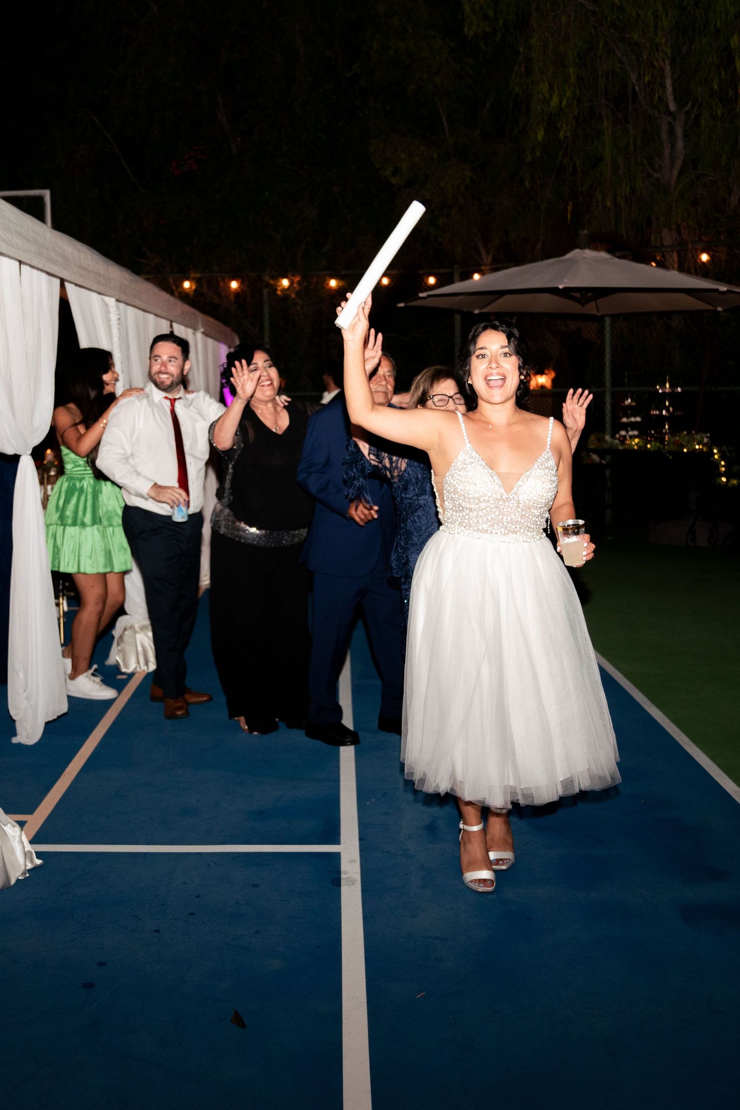 Bride dancing energetically on blue dance floor at outdoor evening reception.