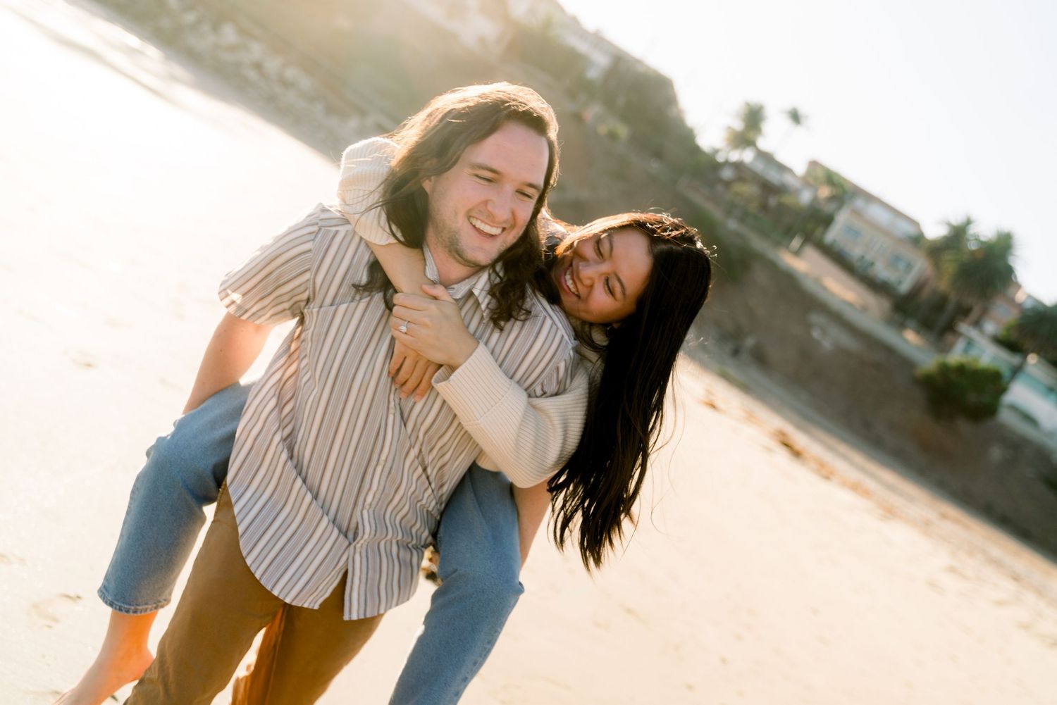 Two friends laugh and enjoy a playful piggyback ride on the beach during golden hour.