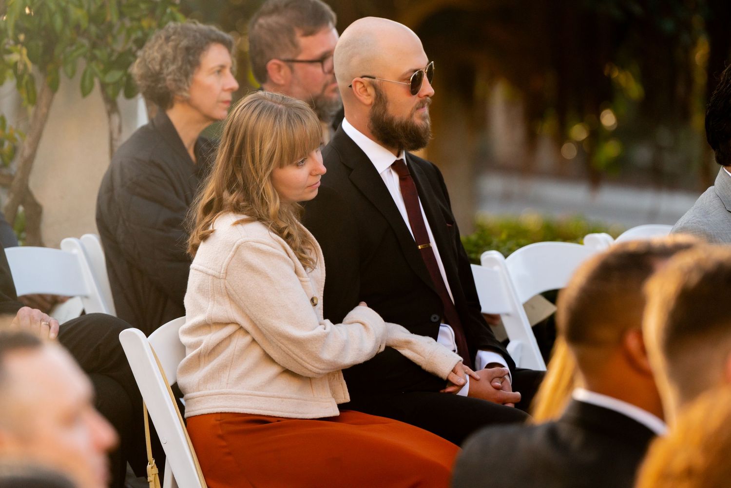 Wedding guests seated in white folding chairs during an outdoor ceremony at dusk.