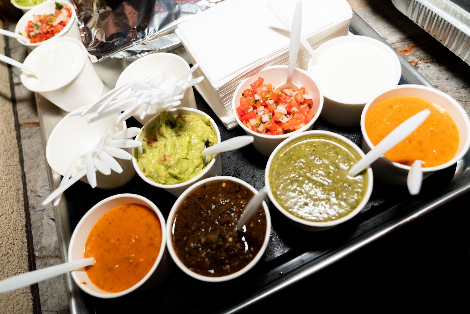 Colorful array of Mexican salsas and dips served in white bowls on dark tray.