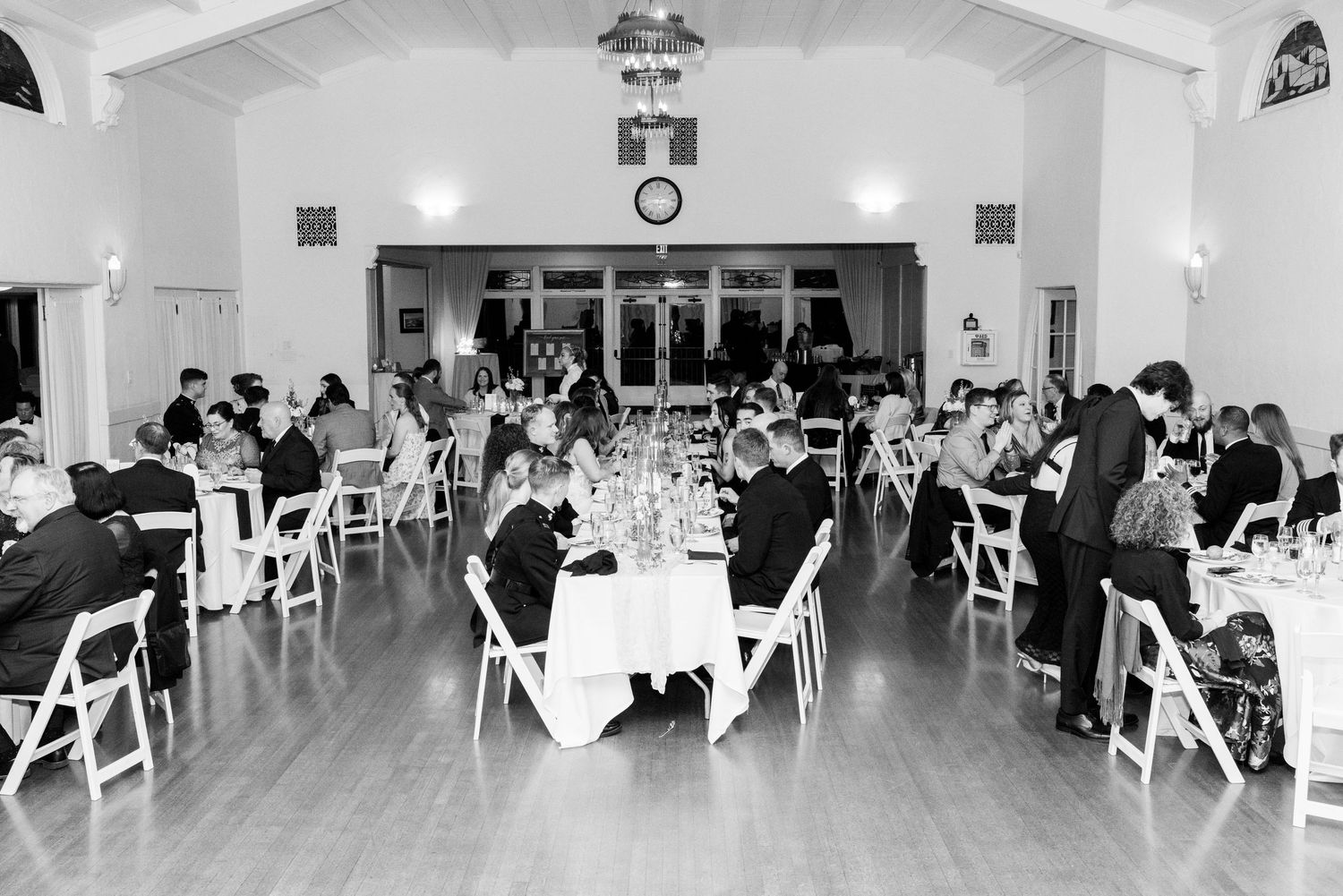 Wedding reception in a bright hall with guests seated at round tables with white tablecloths.
