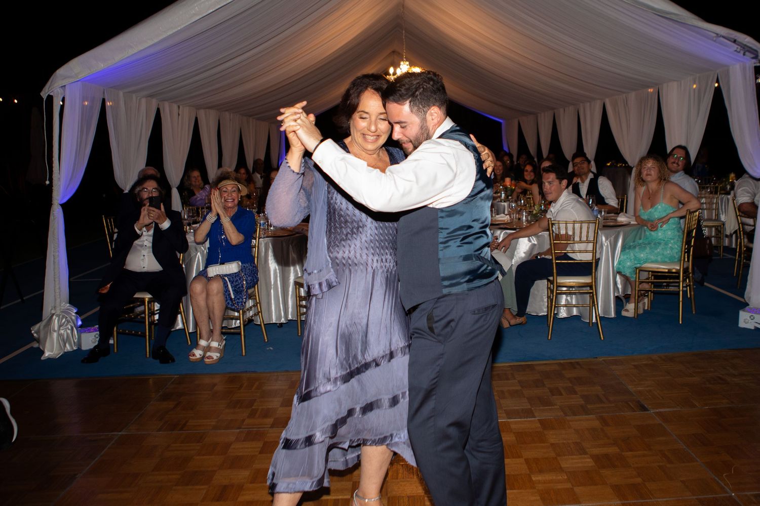 Couple shares an intimate dance under an elegant white tent at their evening wedding reception.