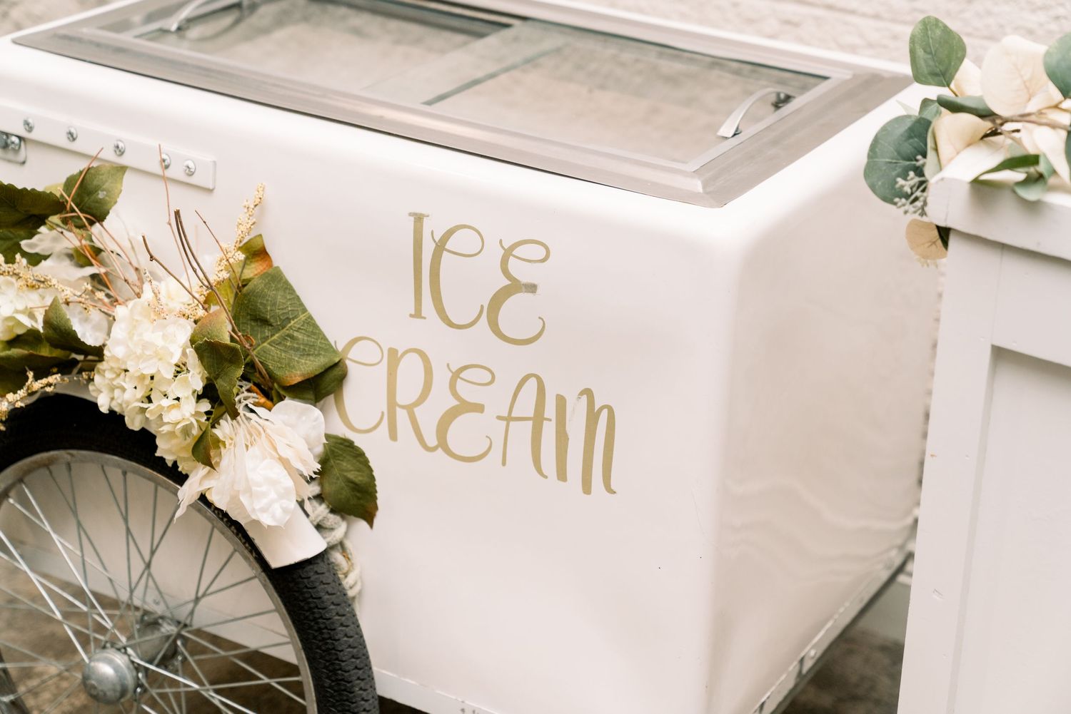 Vintage white ice cream cart with gold lettering decorated with floral arrangements.
