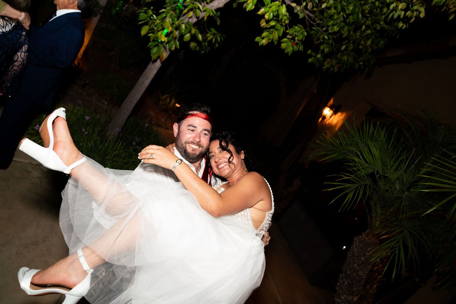 A groom carries his bride while dancing during their wedding celebration at night.