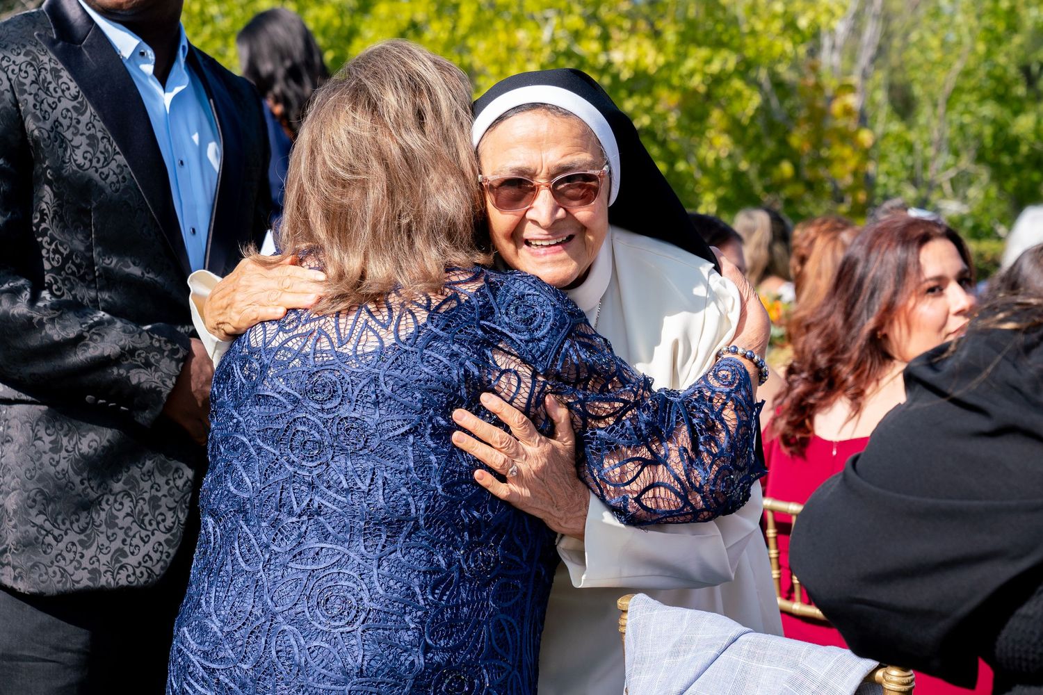Attendees share warm embraces during an outdoor wedding reception.