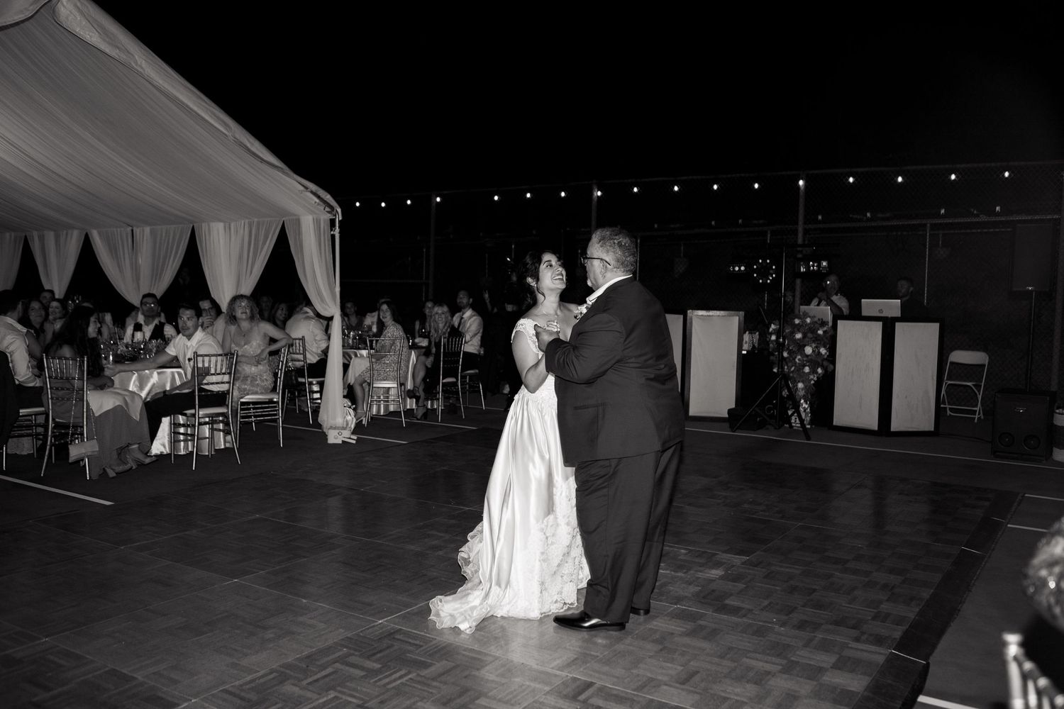 Couple sharing first dance under tent at evening wedding reception with string lights.