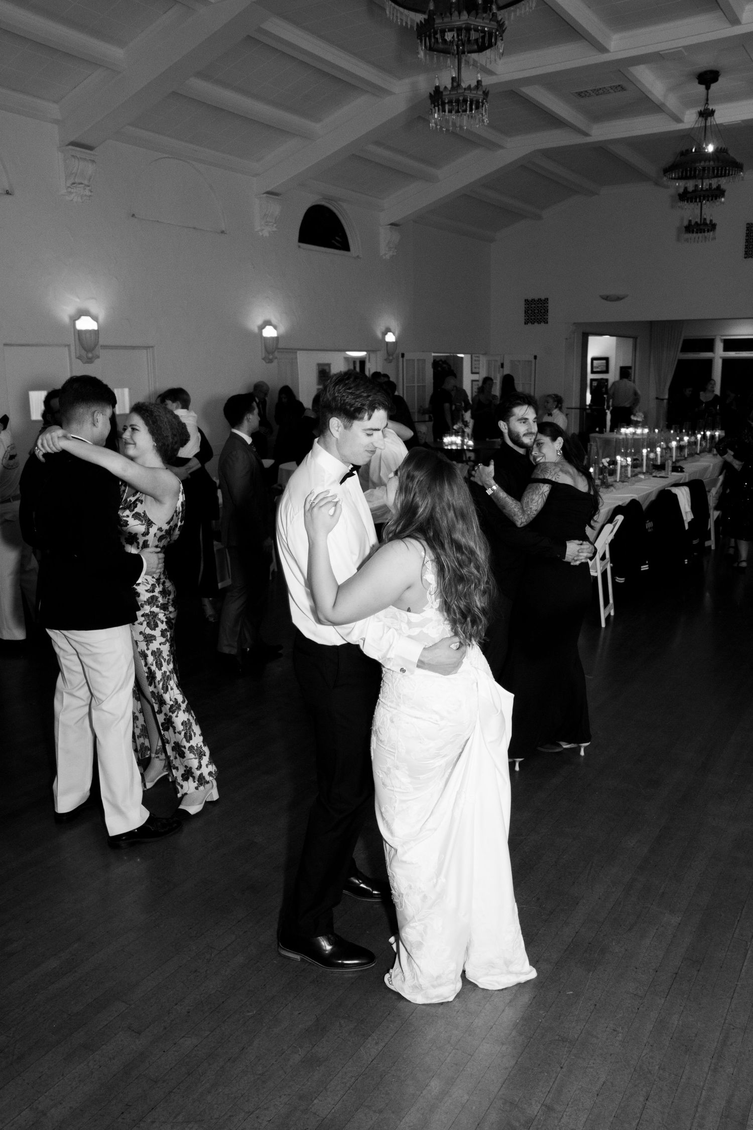 Couples slow dancing on wooden ballroom floor at elegant wedding reception.