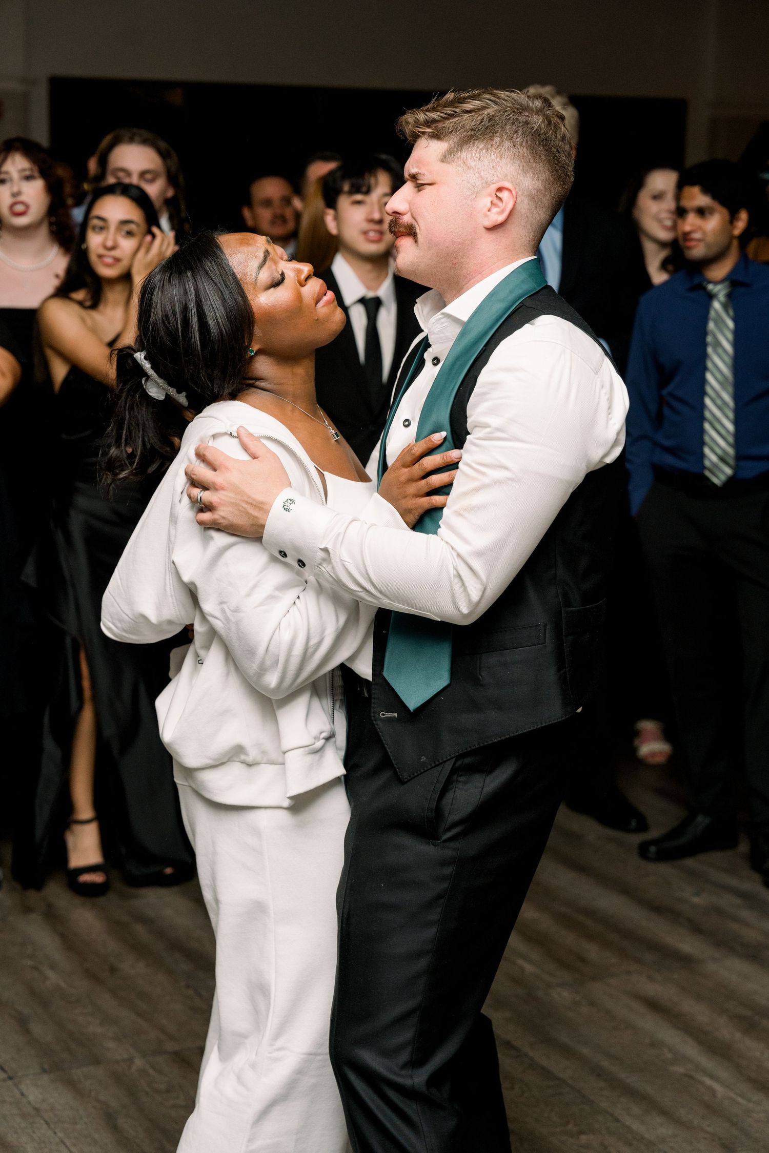 A couple sharing an intimate dance moment during a wedding reception with guests in the background.
