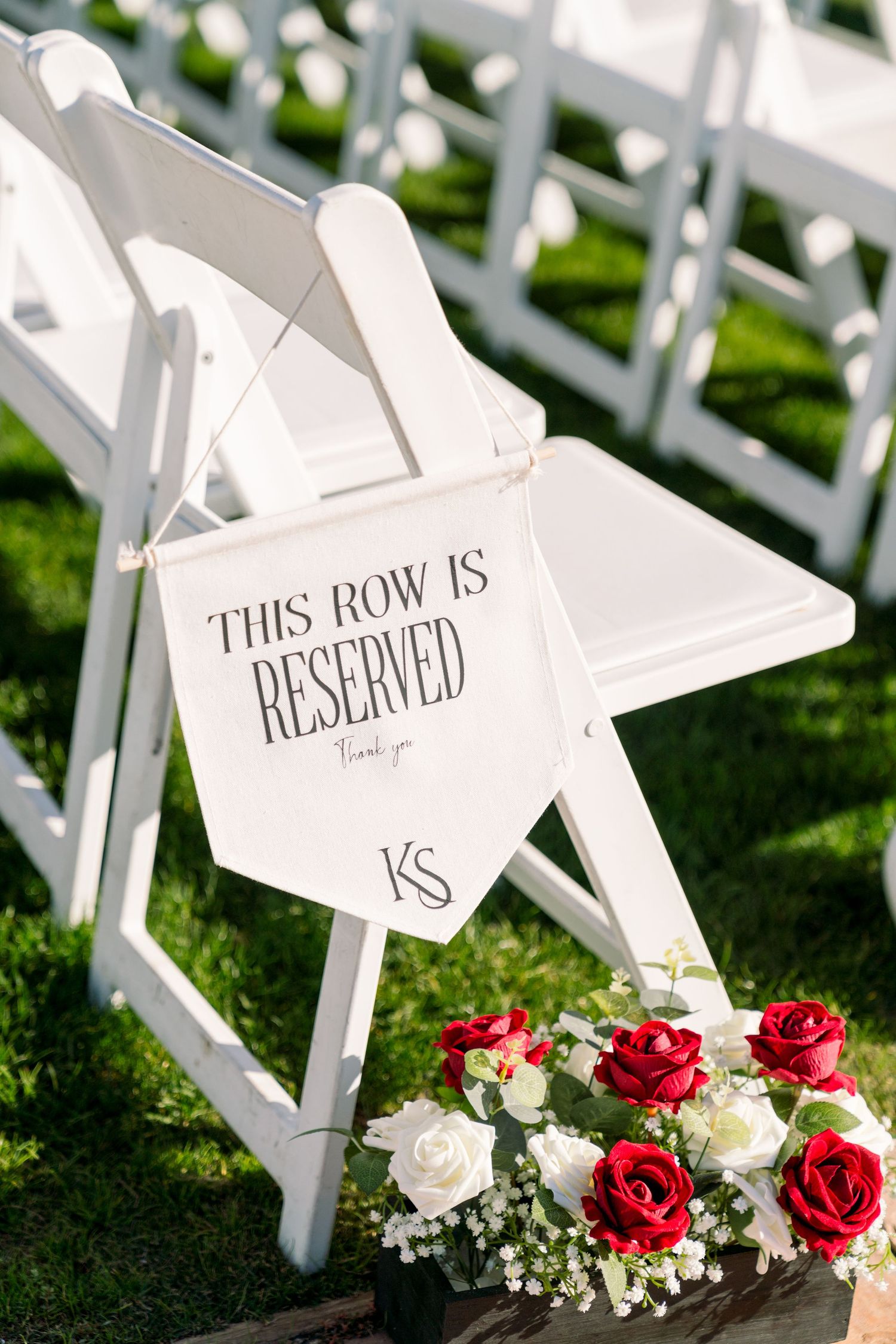 White wedding ceremony chair with 'Reserved' sign and red and white roses floral arrangement.