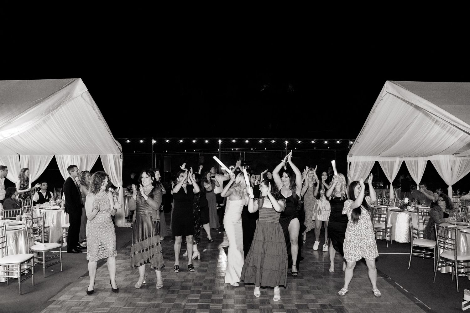 Wedding guests dancing under white tents at night in black and white photography.