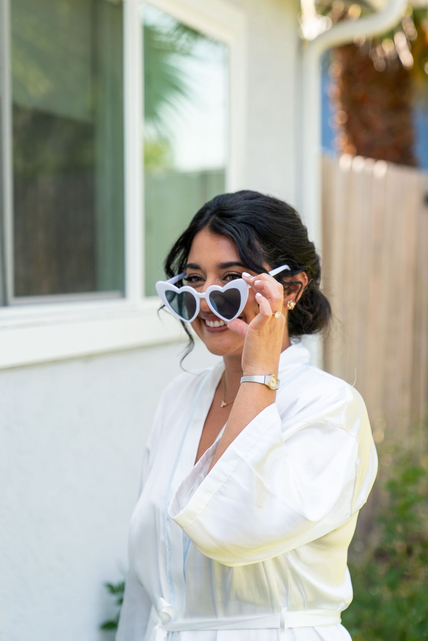A picture of someone wearing heart-shaped sunglasses and a white shirt while posing against a white wall.