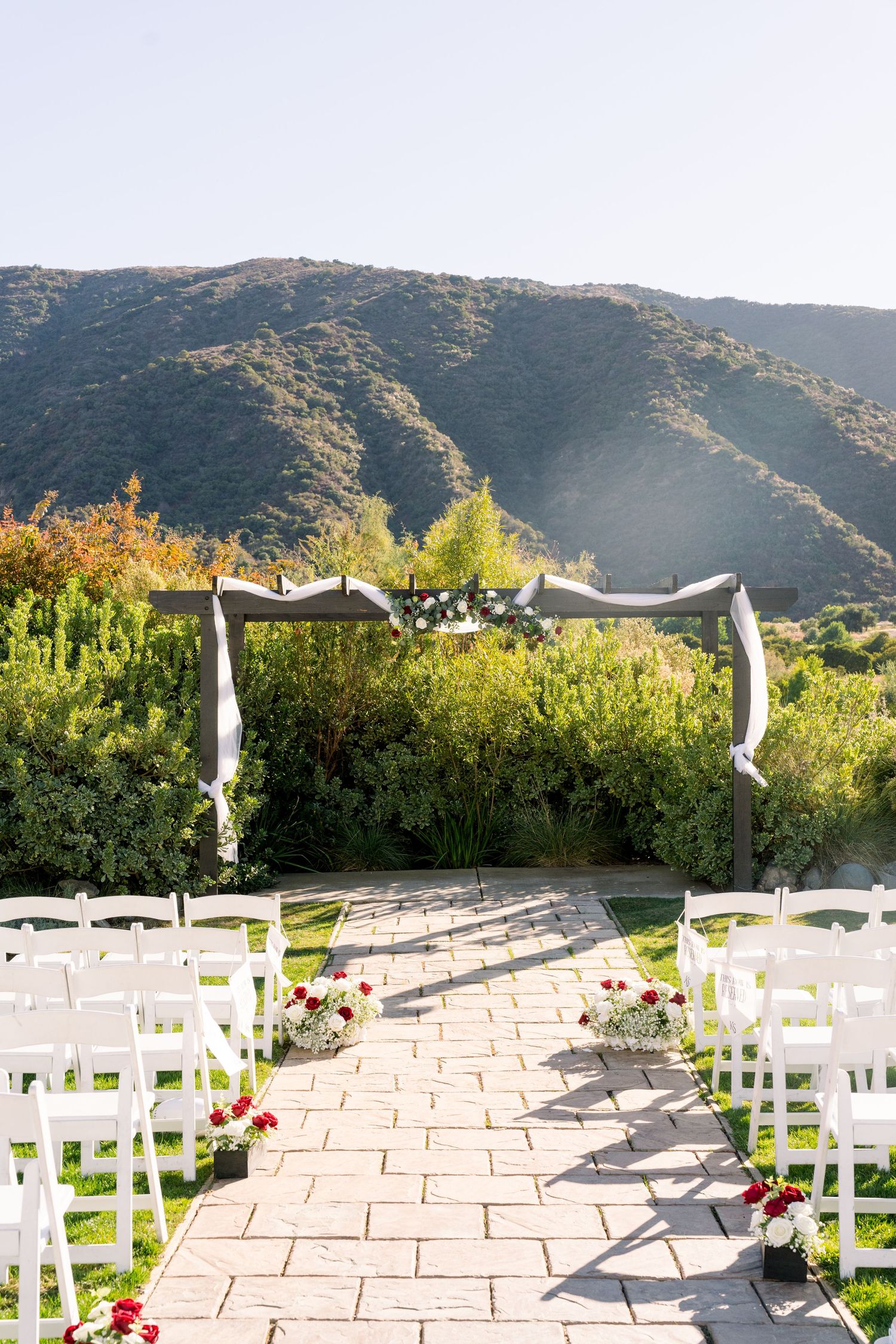 Wedding ceremony setup with white chairs and fabric arch against mountain backdrop.