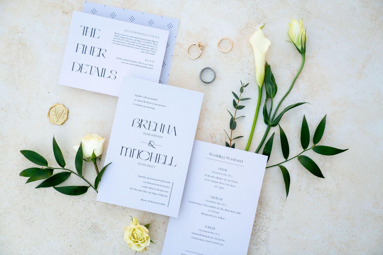 Minimalist white wedding invitation suite with yellow roses and green foliage leaves displayed on light fabric.