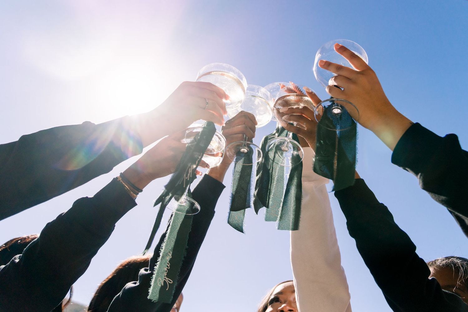 Hands raising bottles against sunlight in celebratory toast.