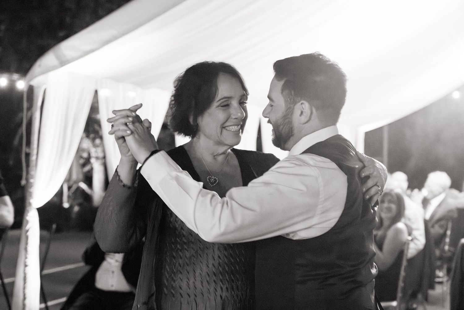 Black and white photo captures joyful couple dancing together at their wedding reception.