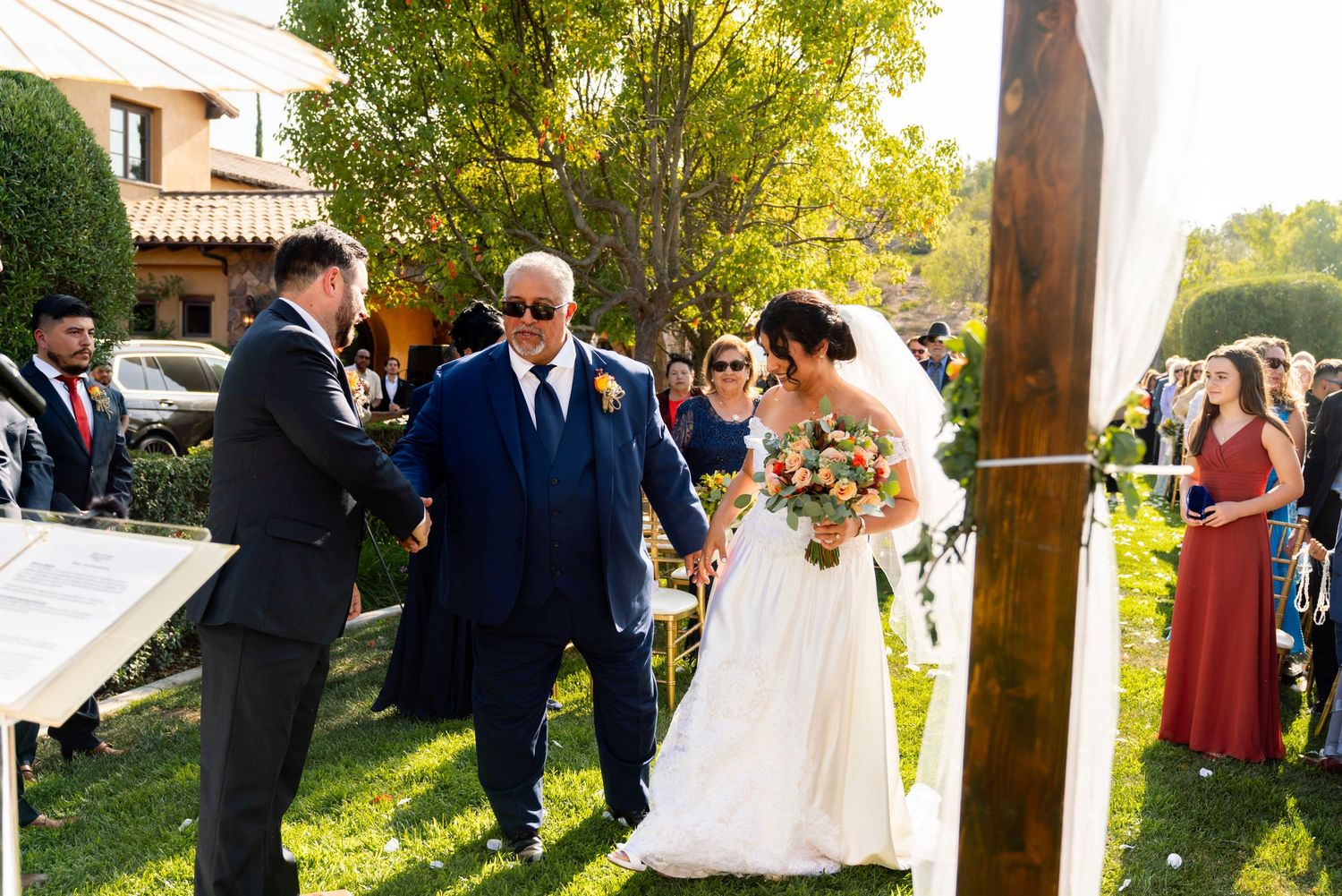 An outdoor wedding ceremony taking place on a sunny lawn with guests looking on.