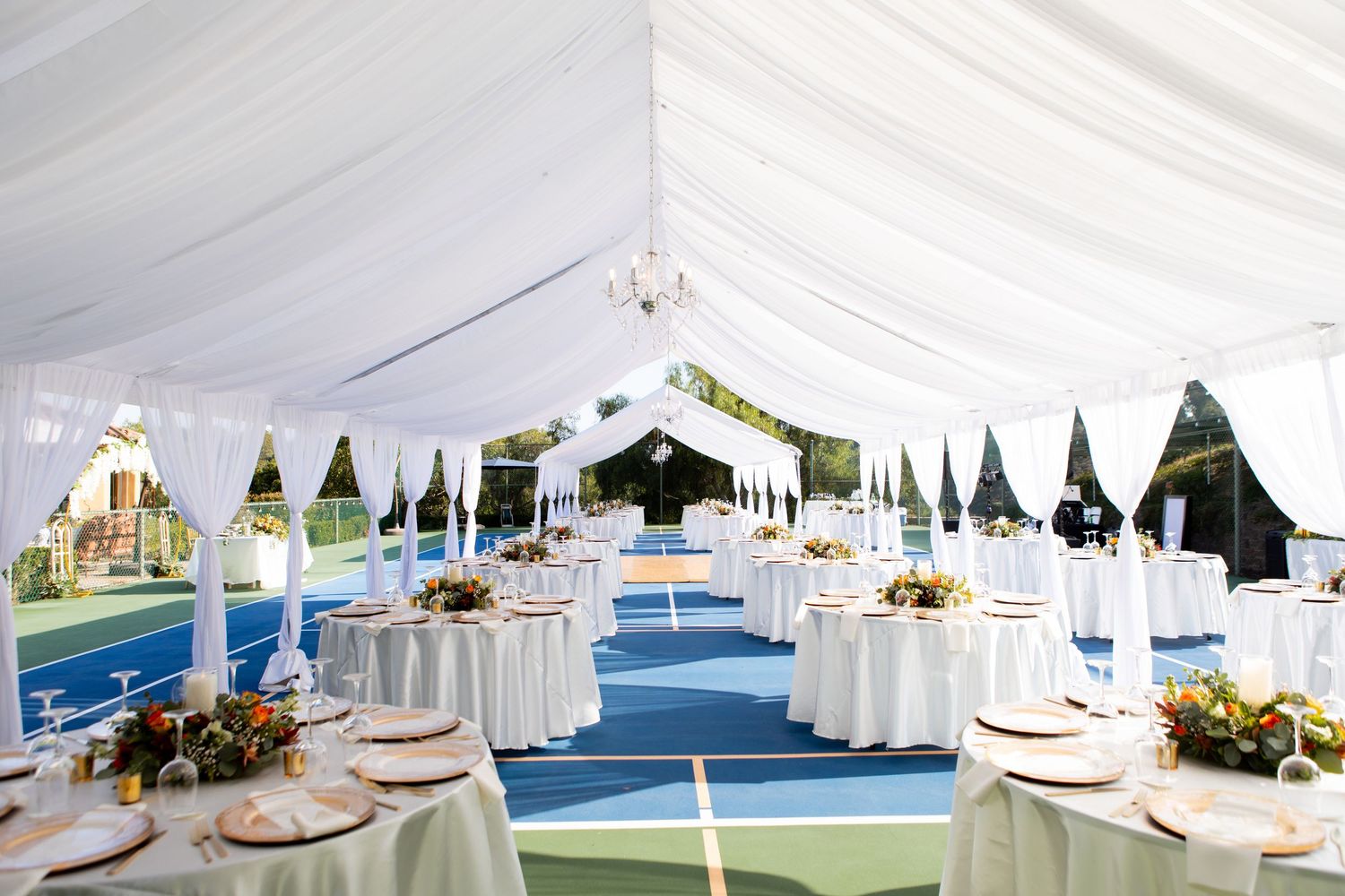 Elegant white tent reception setup with round tables and blue carpet runner.