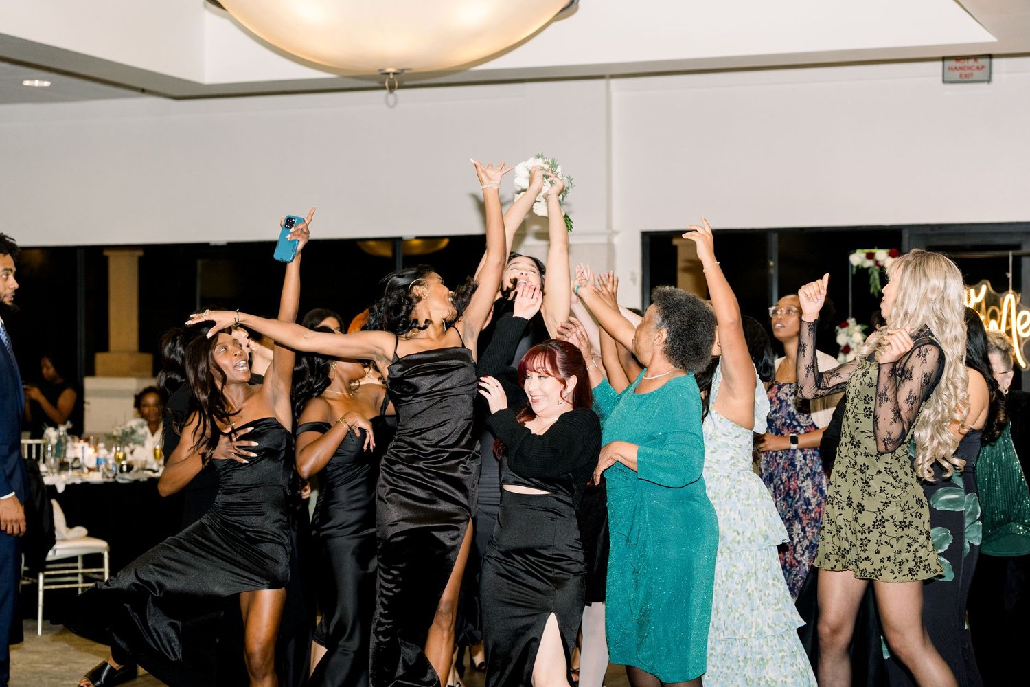 Wedding reception guests reaching up to catch the bouquet toss.