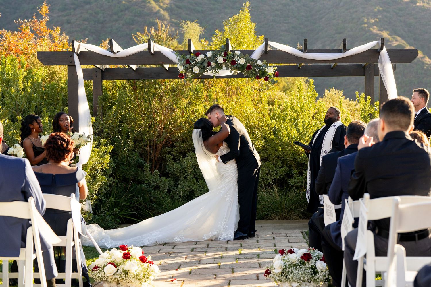 Couple sharing first dance at outdoor wedding ceremony with white canopy and autumn foliage.