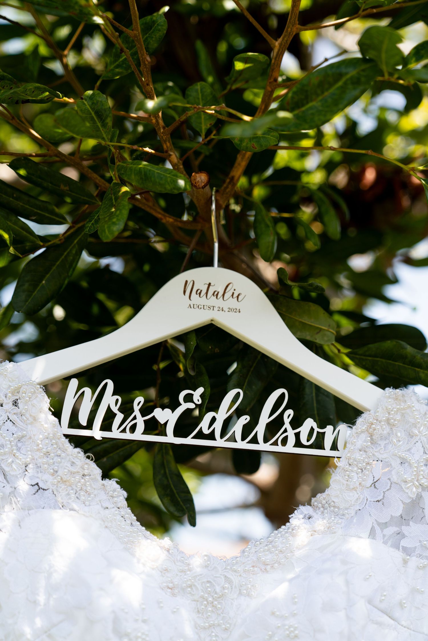 Custom wedding dress hanger with 'Mrs. Edelson' text displayed against green foliage.