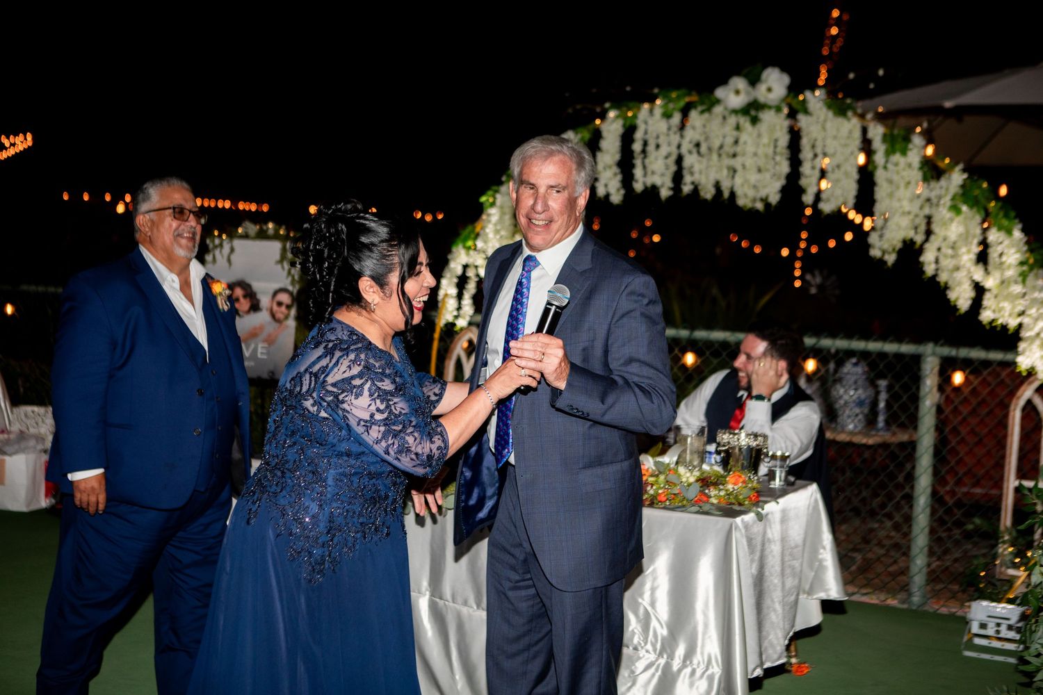 Evening wedding reception with guests dancing under floral arch and string lights.