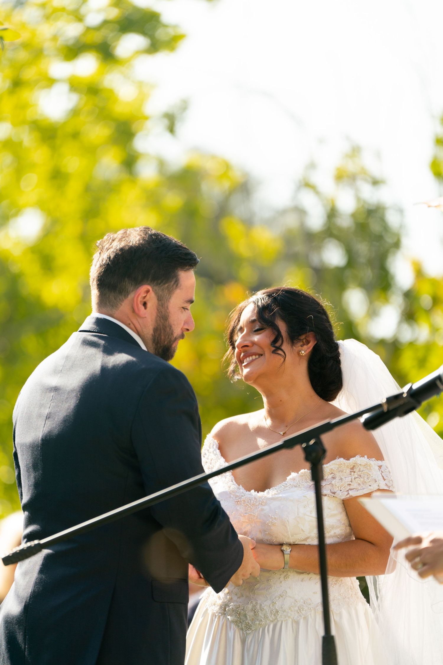 A tender moment between newlyweds during their outdoor wedding ceremony with a microphone stand visible.