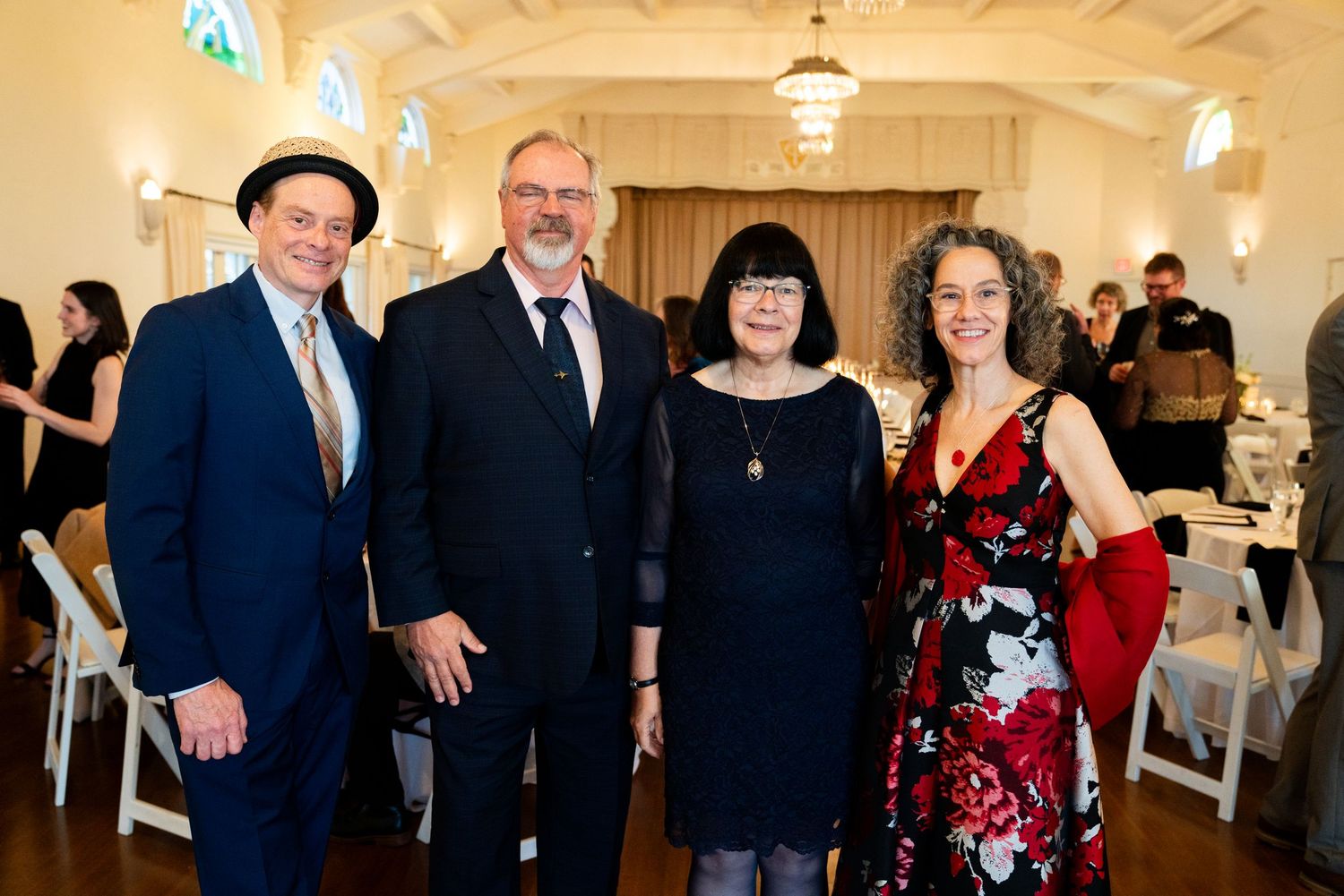 Four guests posing together for a formal event photo in an elegantly decorated venue with chandeliers.
