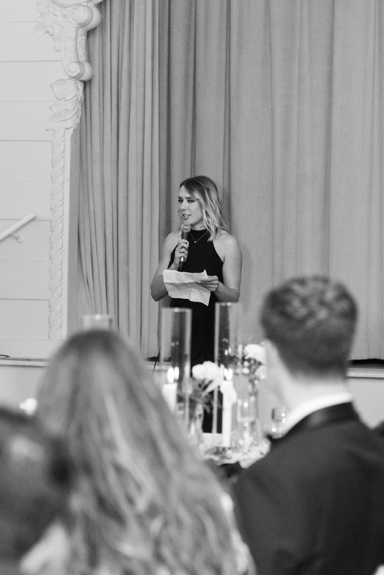 Guest speaker delivering speech at formal wedding reception in elegant ballroom setting.