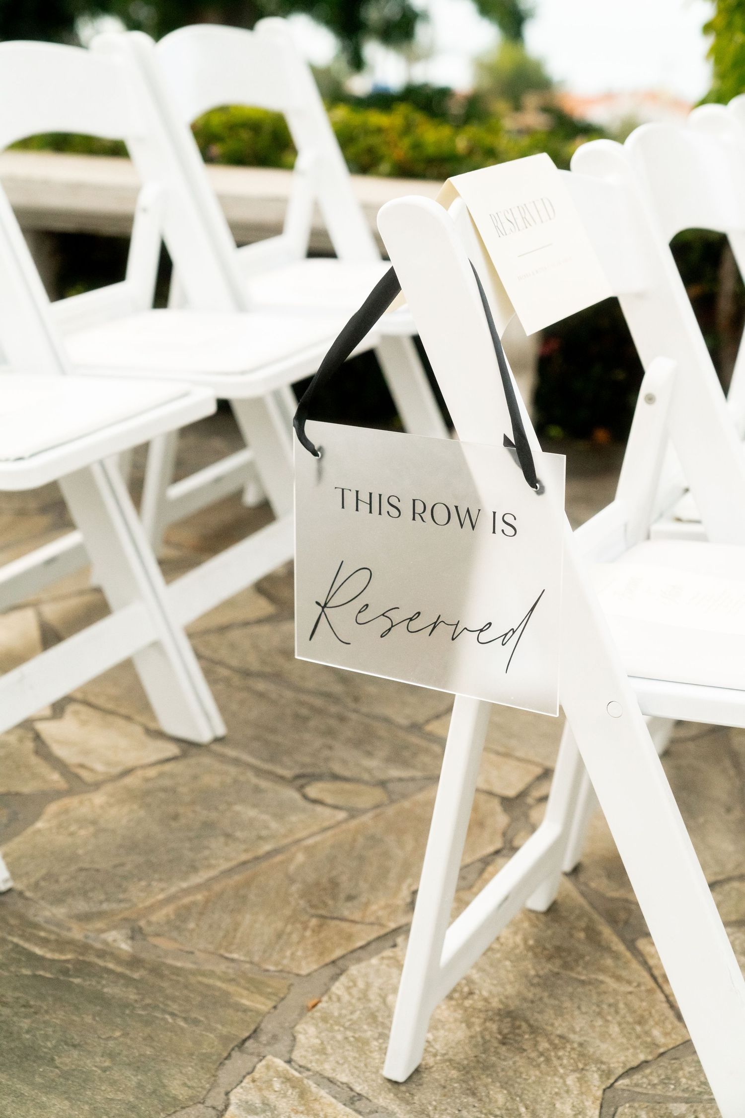 White folding chairs with 'Reserved' signs line up at an outdoor wedding ceremony venue.