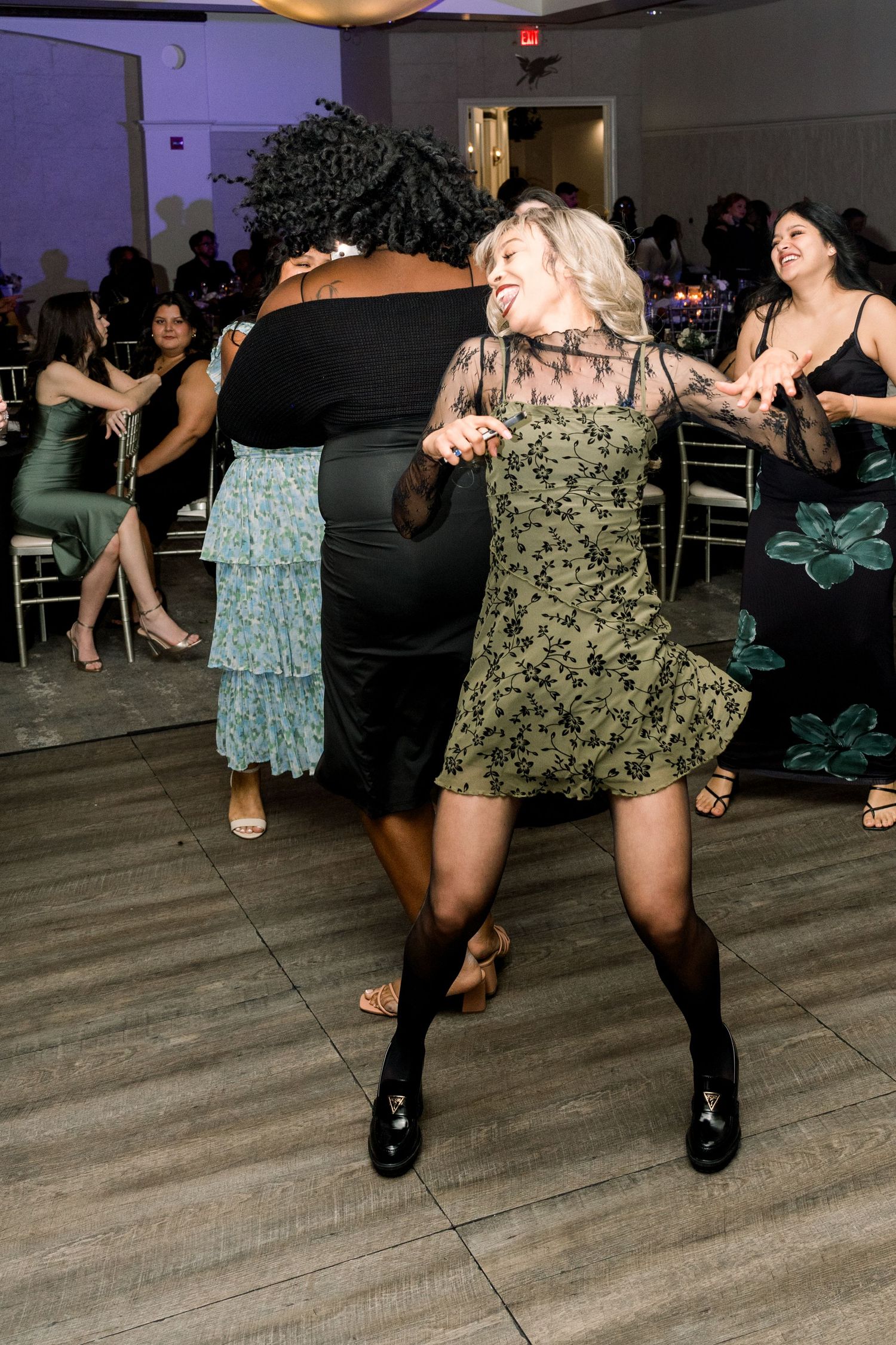 Wedding reception guests dancing energetically on a wooden dance floor under purple lighting.