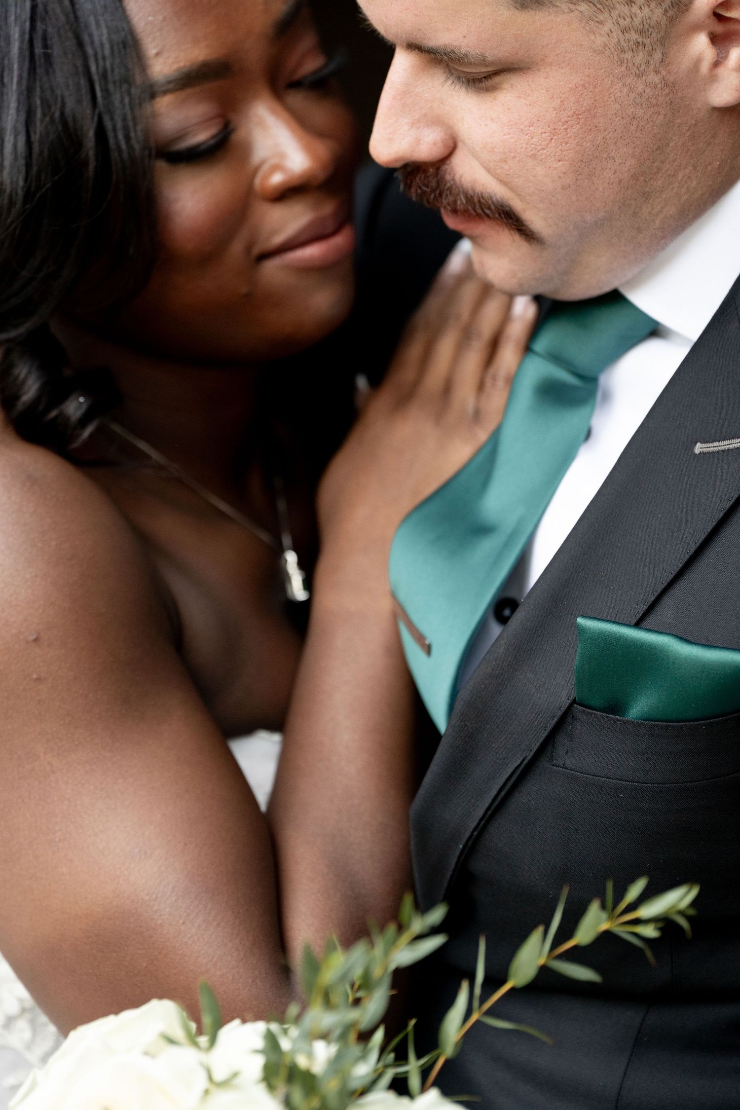 Close romantic embrace of couple at wedding with groom in black suit and emerald green tie and pocket square.