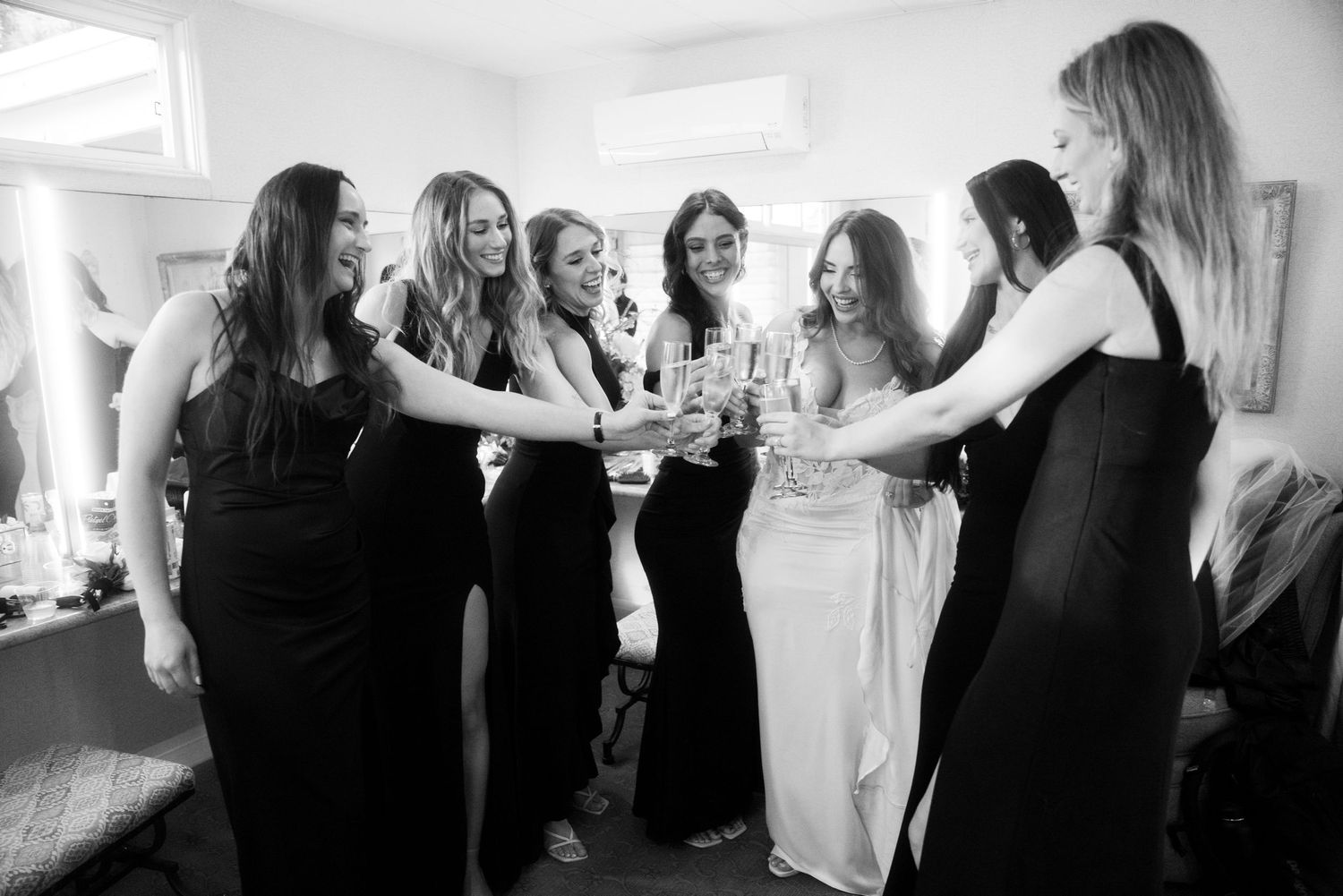 A group in black and white formal dresses raise glasses in a celebratory toast during a special event.
