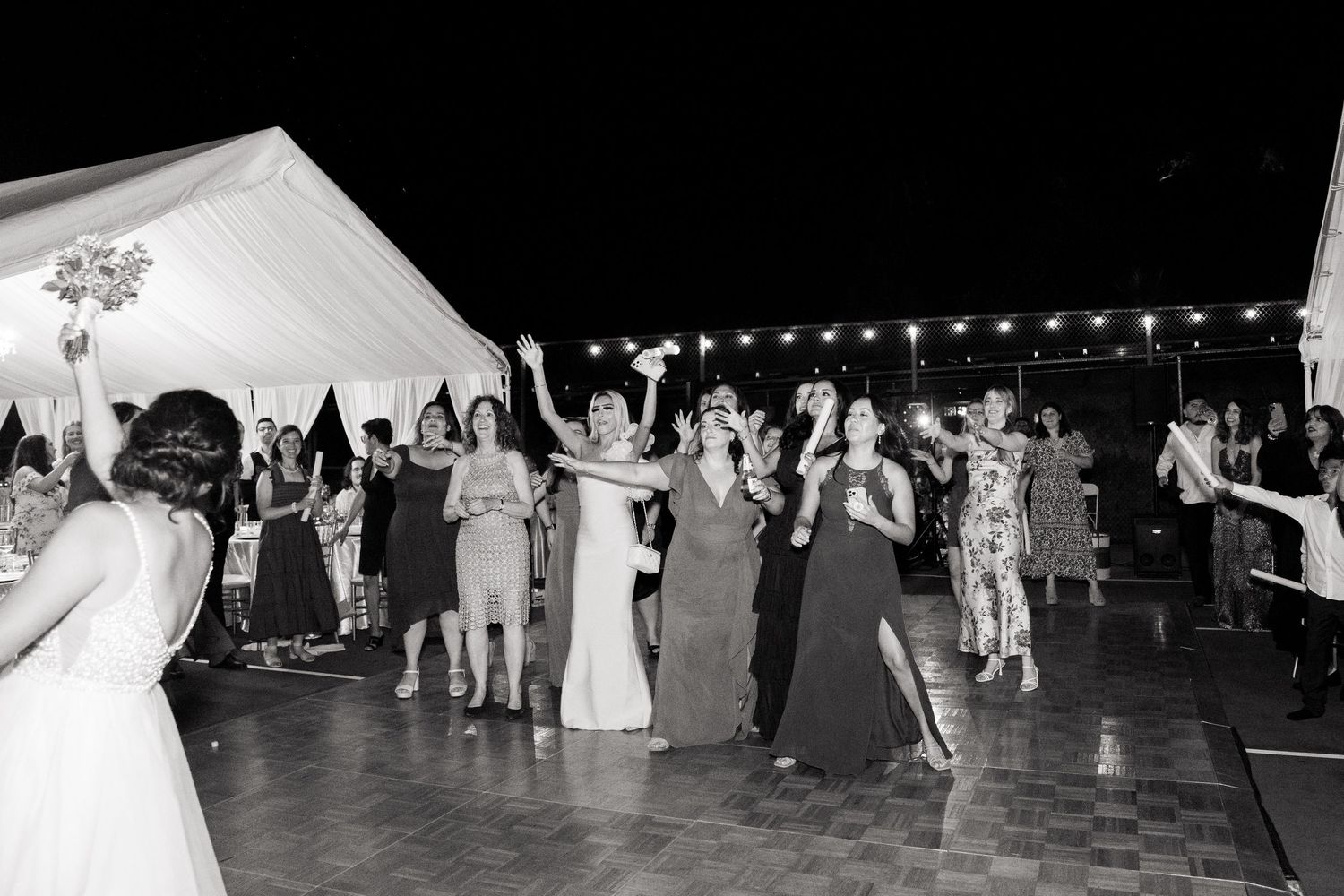 Wedding guests dancing and celebrating on an outdoor dance floor under a white tent at night.