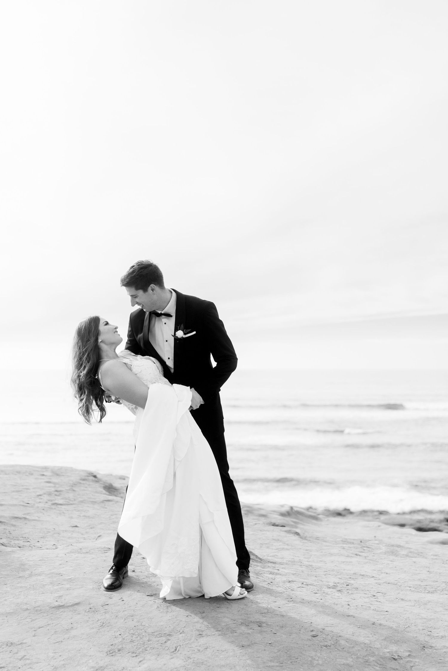 A romantic black and white photo of newlyweds sharing an intimate dance pose on a beach.